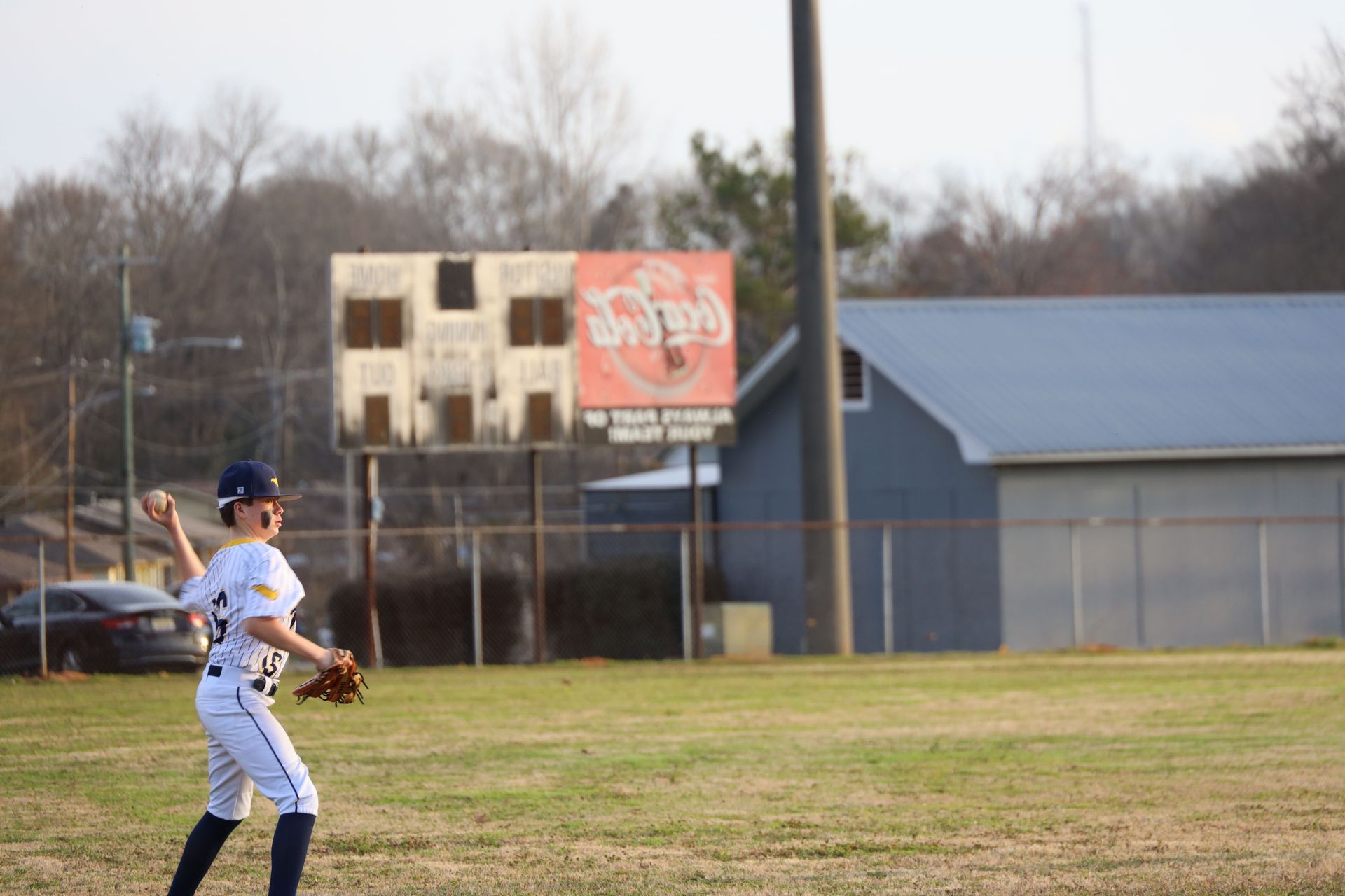 Baseball player in white uniform fields a ball on a grassy field near a blue building