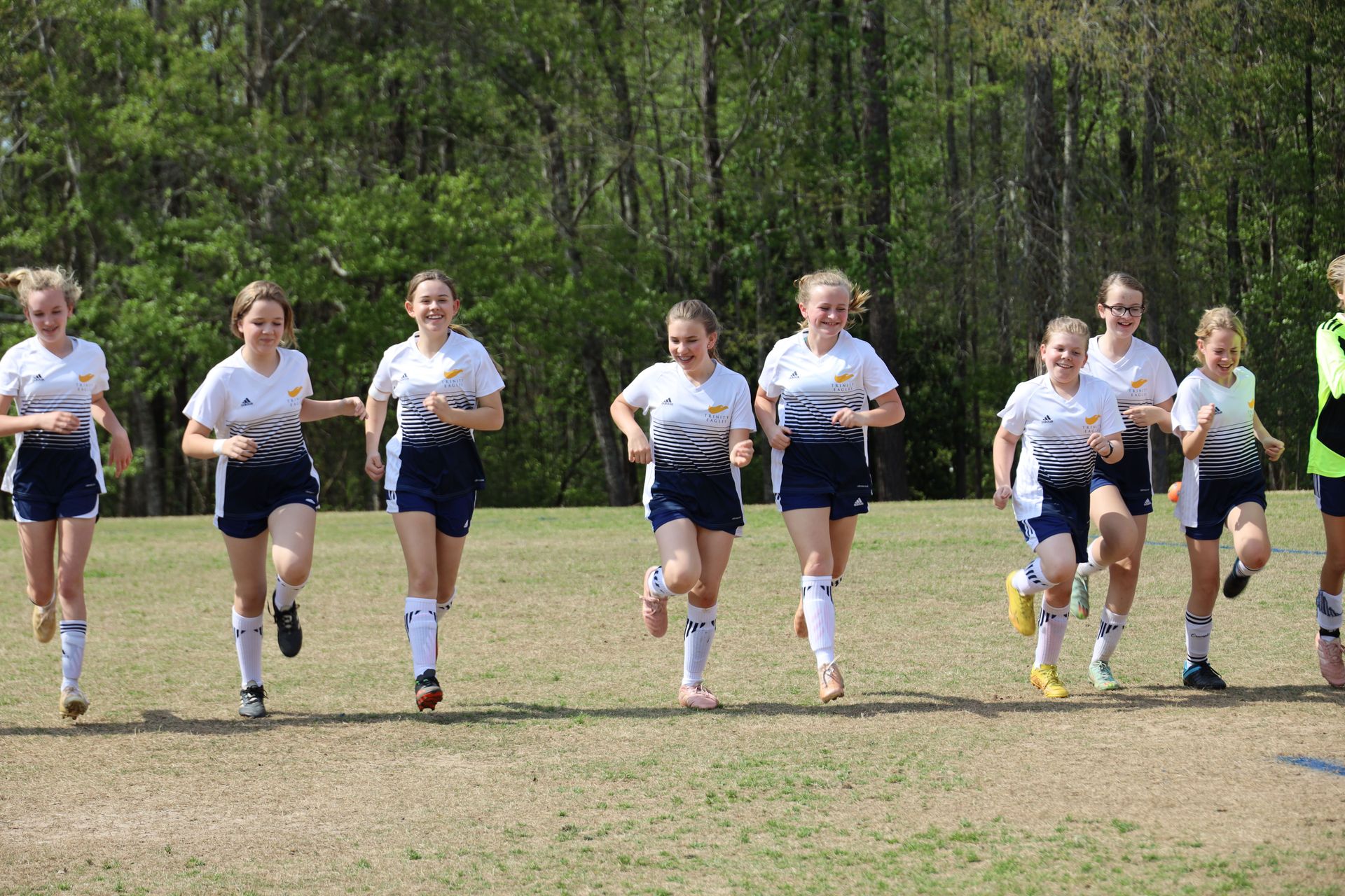 Group of runners in white shirts and navy shorts jogging on a grassy field