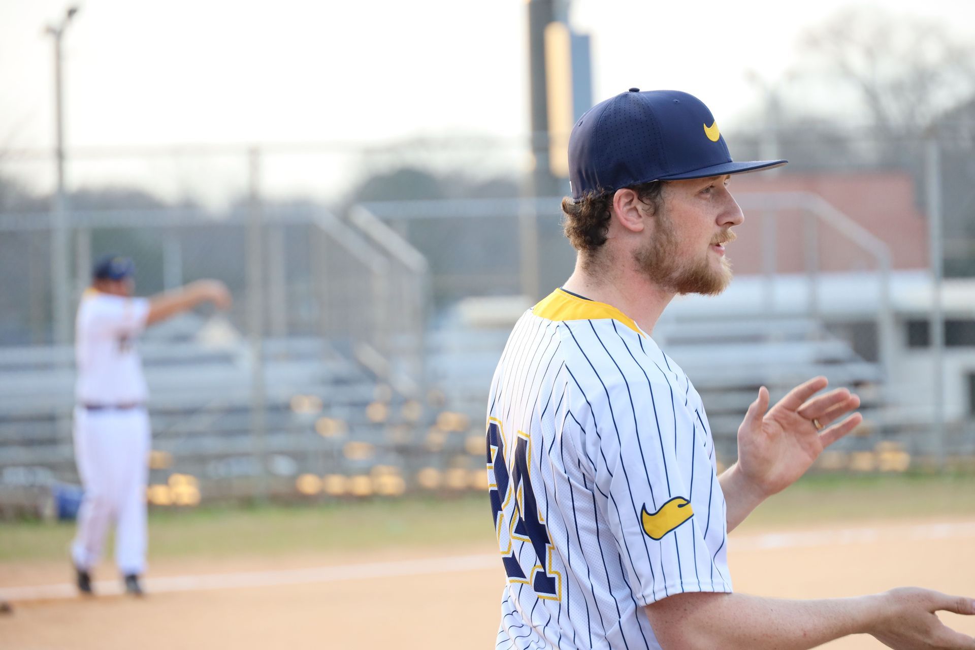 Baseball player in white pinstripes and blue cap claps on the field, with another player blurred in the background.