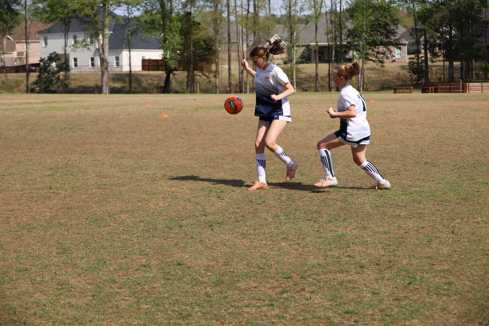 Two people playing soccer on a grassy field, with one kicking the ball near a goal area.