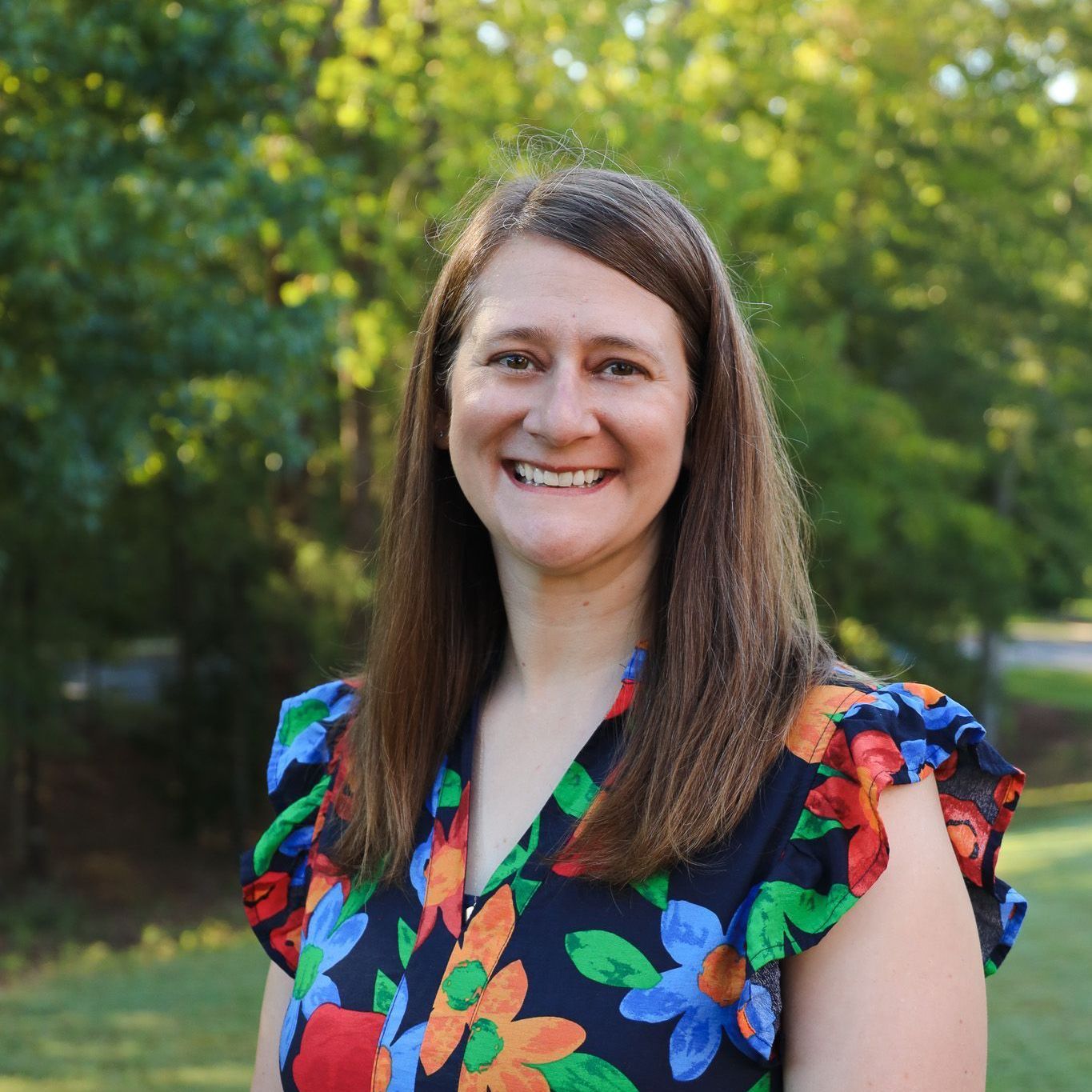 Smiling woman in a colorful floral blouse standing outdoors in a leafy park