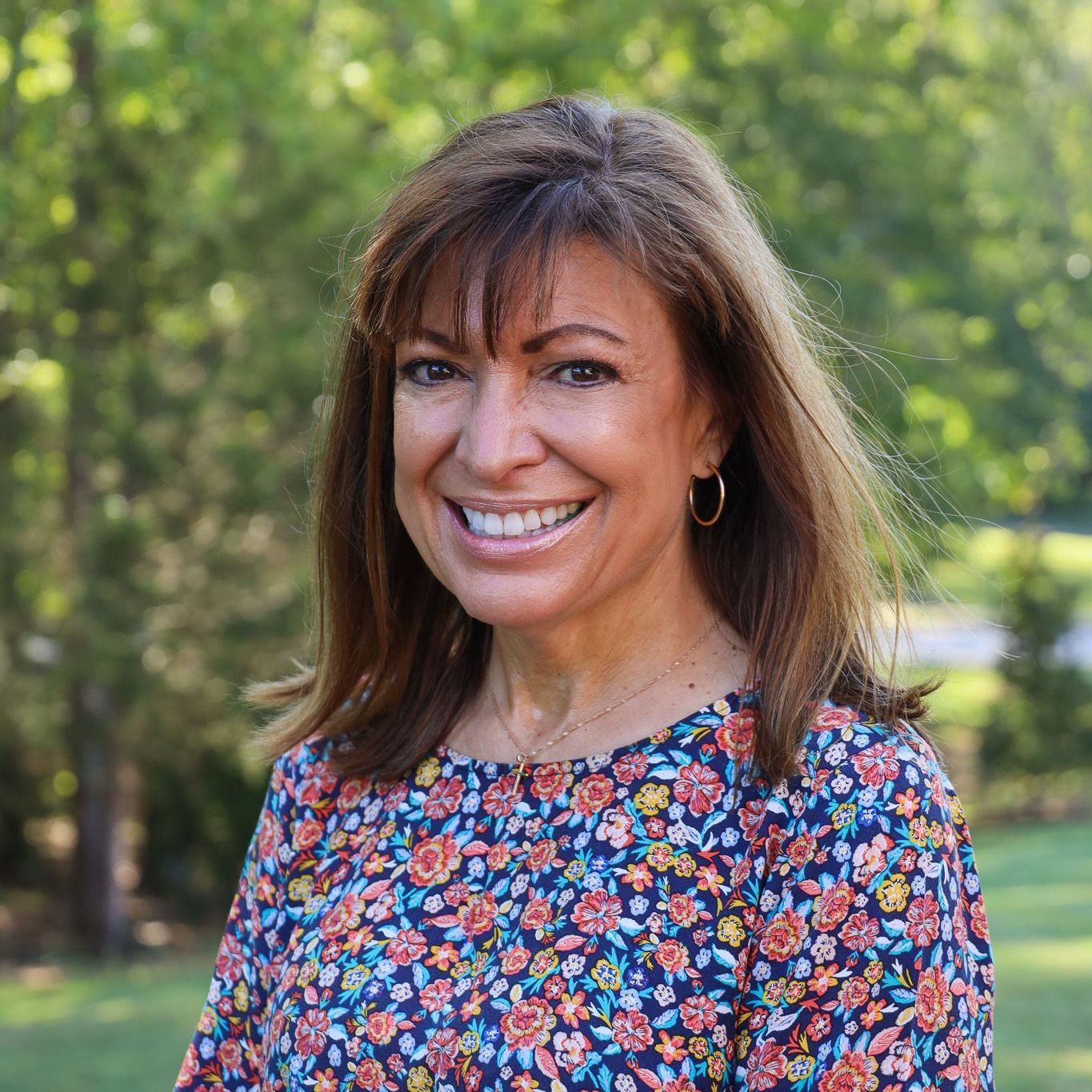 Smiling woman in a floral dress standing outdoors with blurred greenery behind her