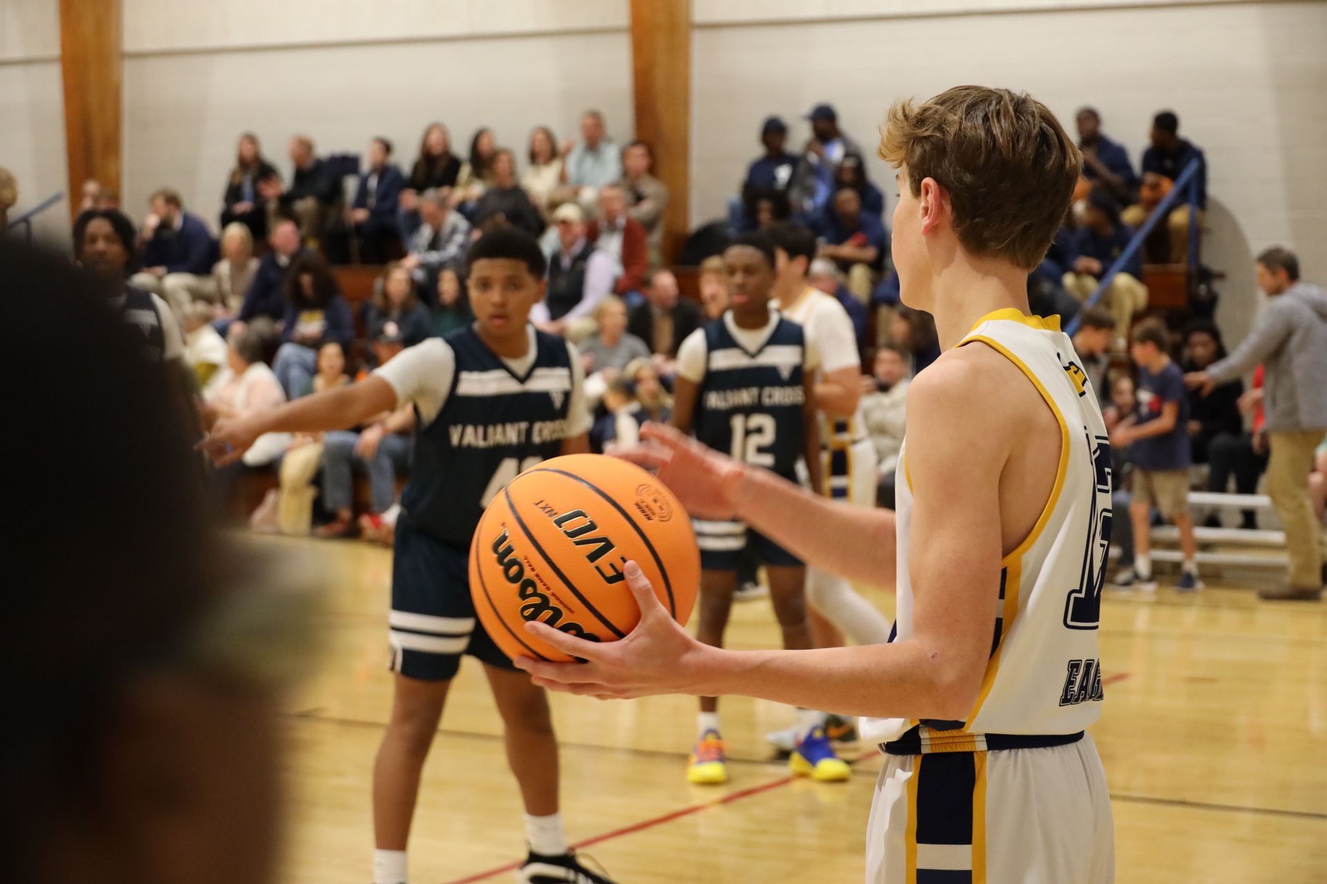 Basketball player holding the ball on court with opponents and spectators in the background
