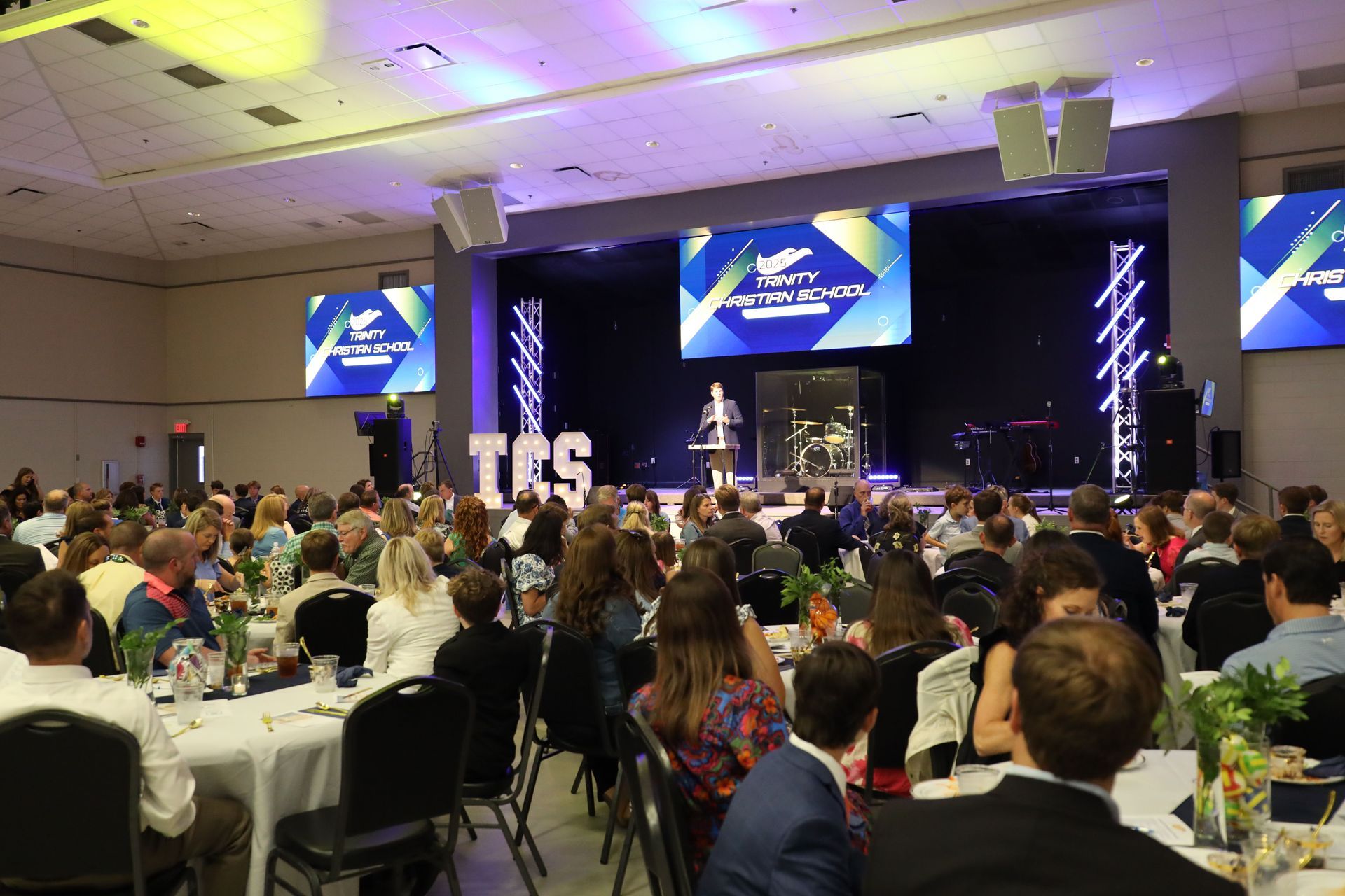 Banquet hall conference with seated audience facing a stage and large presentation screen