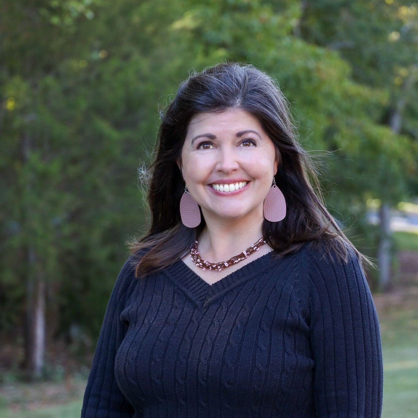 Smiling woman in a dark sweater standing outdoors with trees in the background