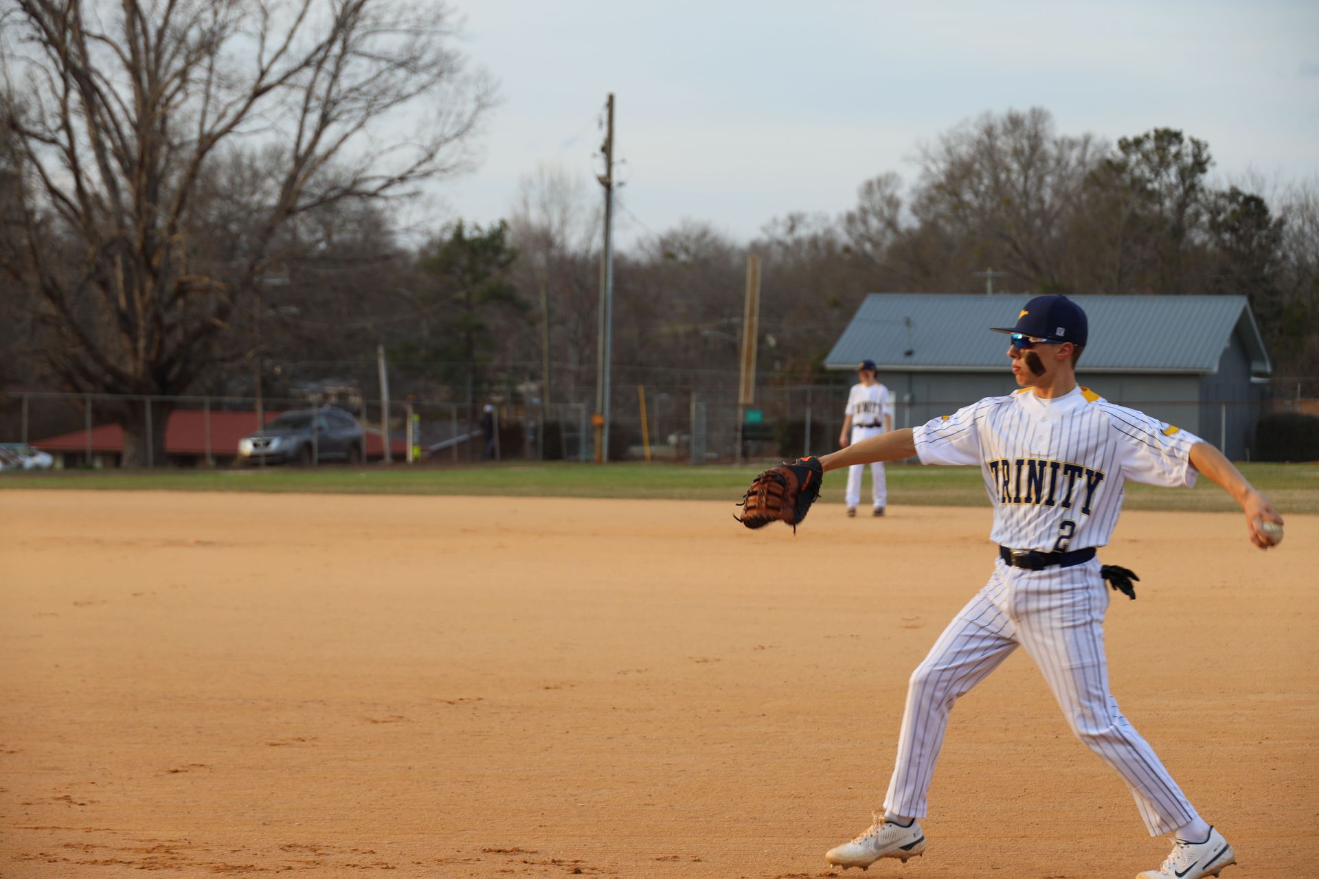 Baseball player in white uniform and blue cap catching a ball on a dirt field