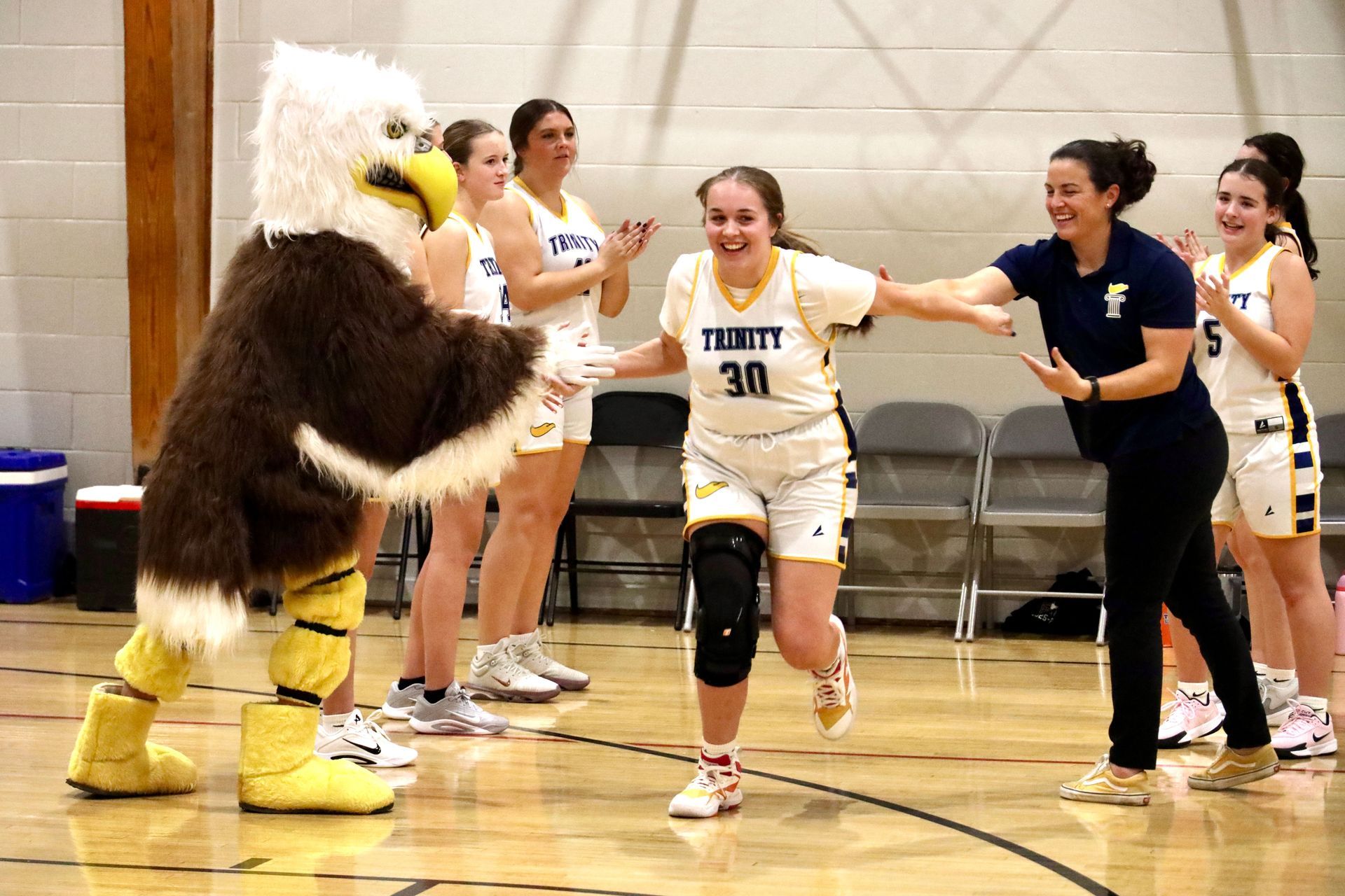 Mascot high-fives smiling basketball player on court while teammates cheer nearby