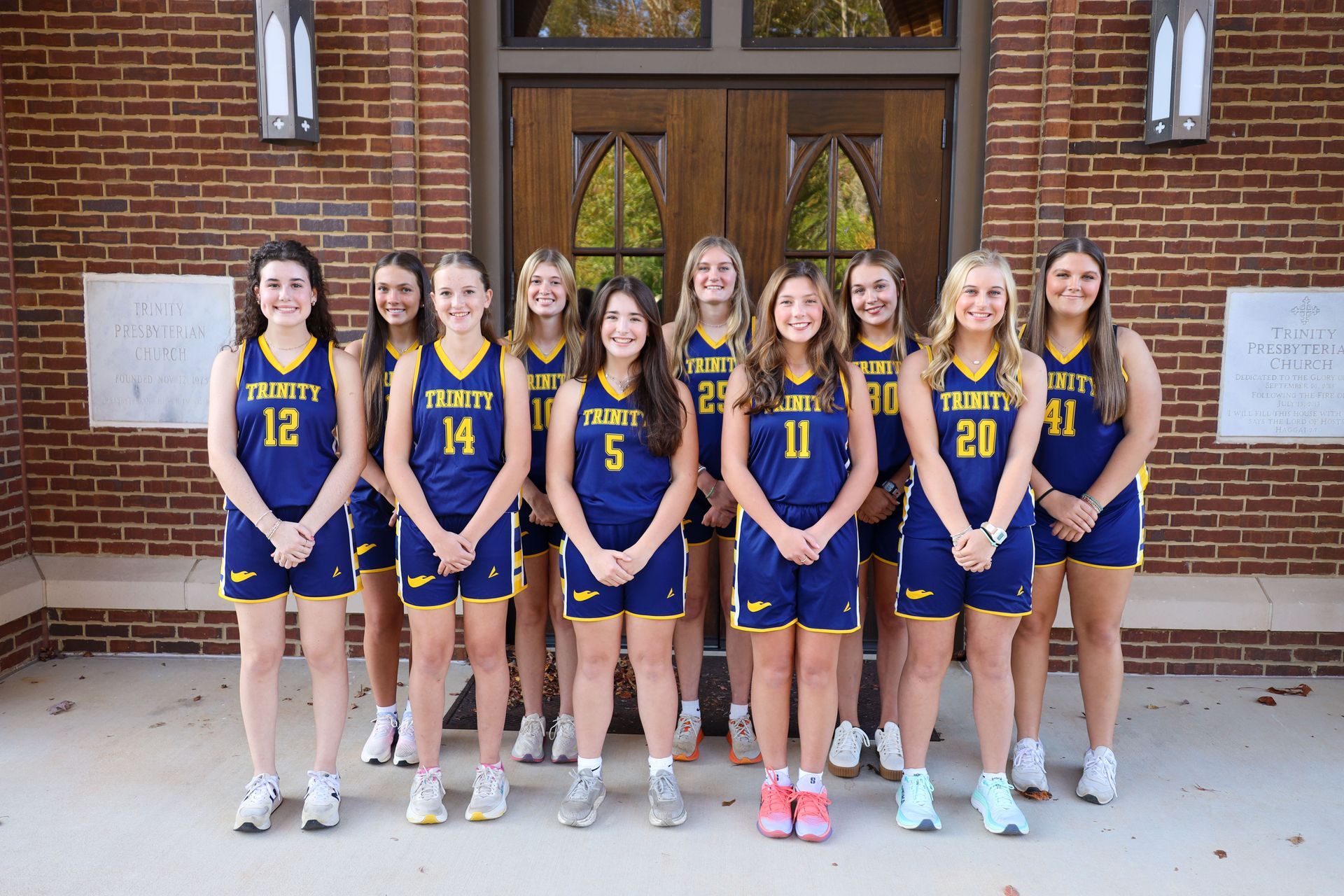 Girls’ basketball team posing in blue and gold uniforms outside a brick building