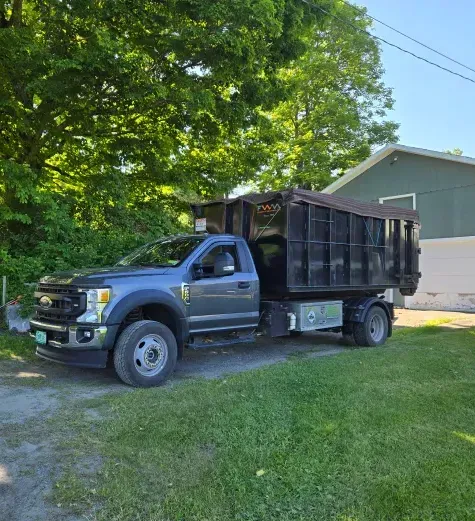 A gray dump truck parked on a driveway with a grassy lawn in front of a green building.