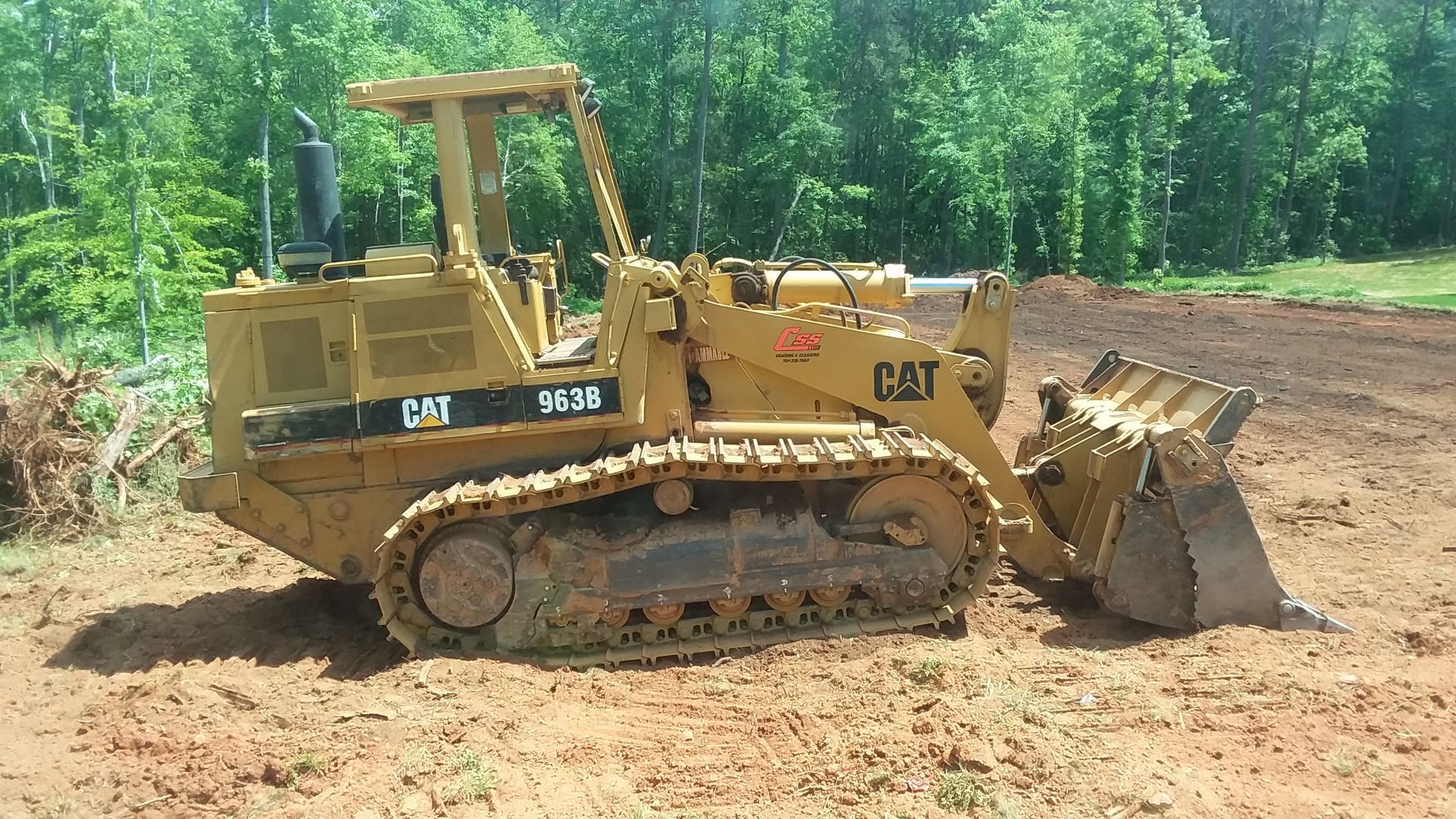 Yellow excavator close-up digging through logs and dirt.