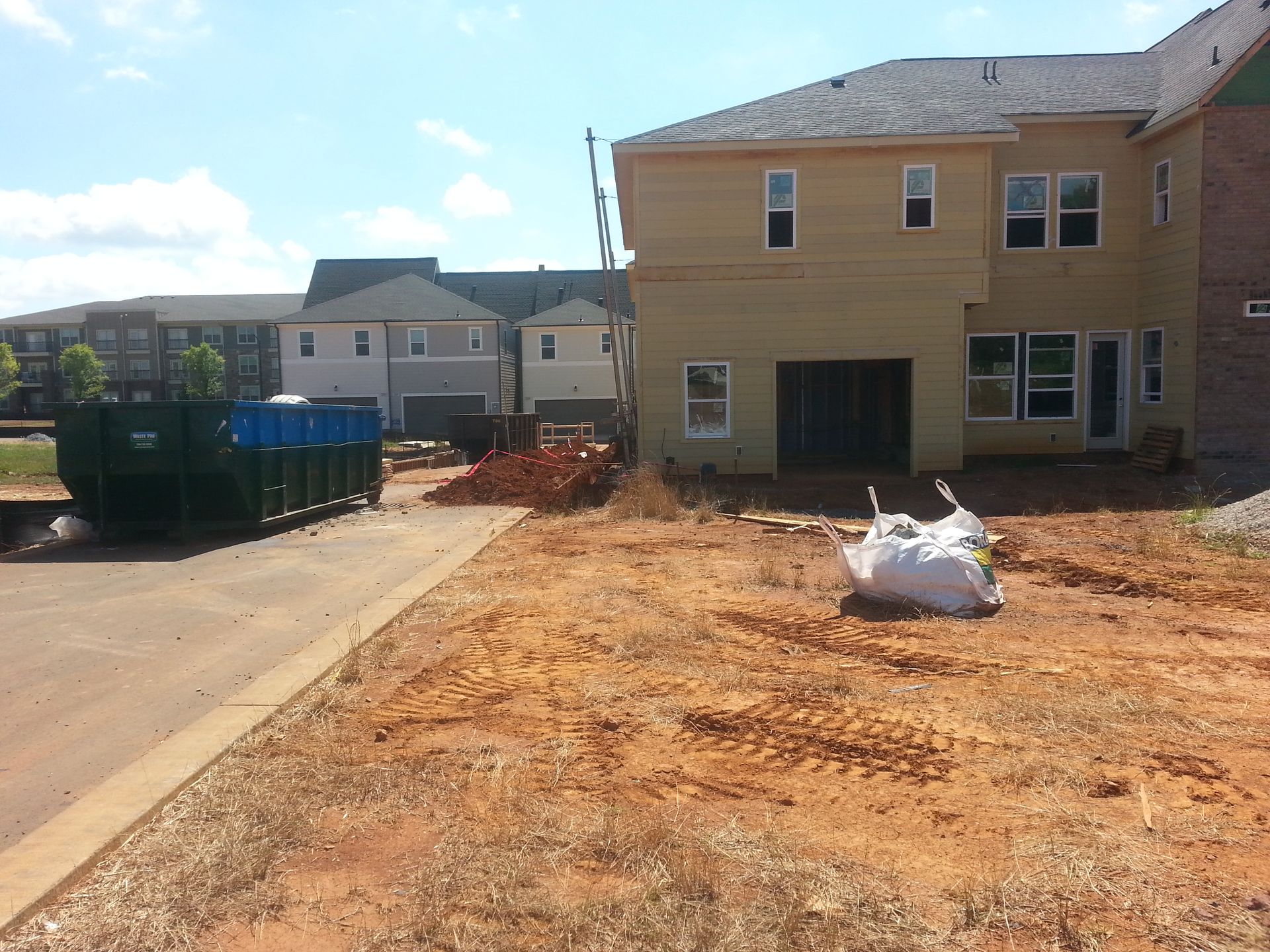 Bulldozer grading red dirt at a construction site near a house.