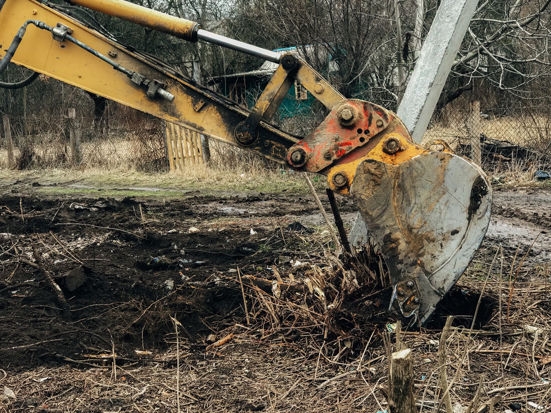 Yellow excavator bucket digging into muddy ground at a wooded construction site