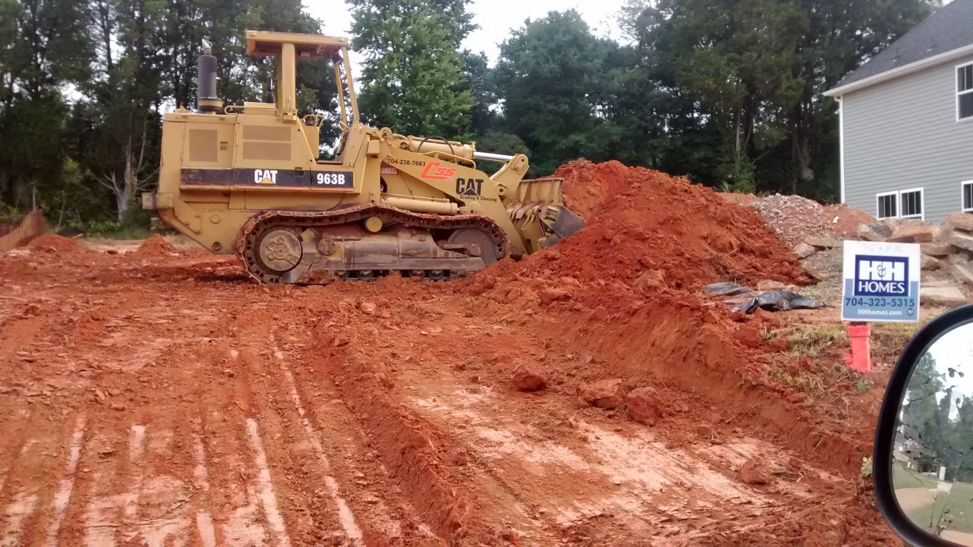 Logs stacked on a construction site with multiple excavators in the background.