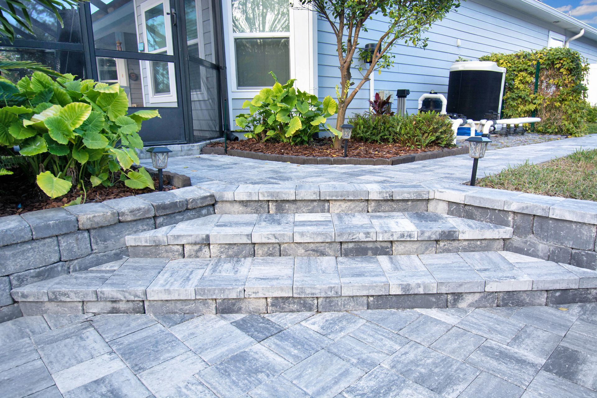 Stone front steps leading to a modern house entry with landscaped plants and gray pavers