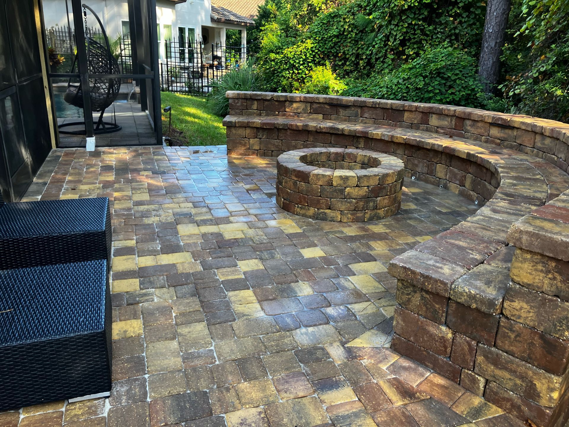 Outdoor patio with a stone fire pit, curved stone seating wall, and dark woven chairs on a paver deck.