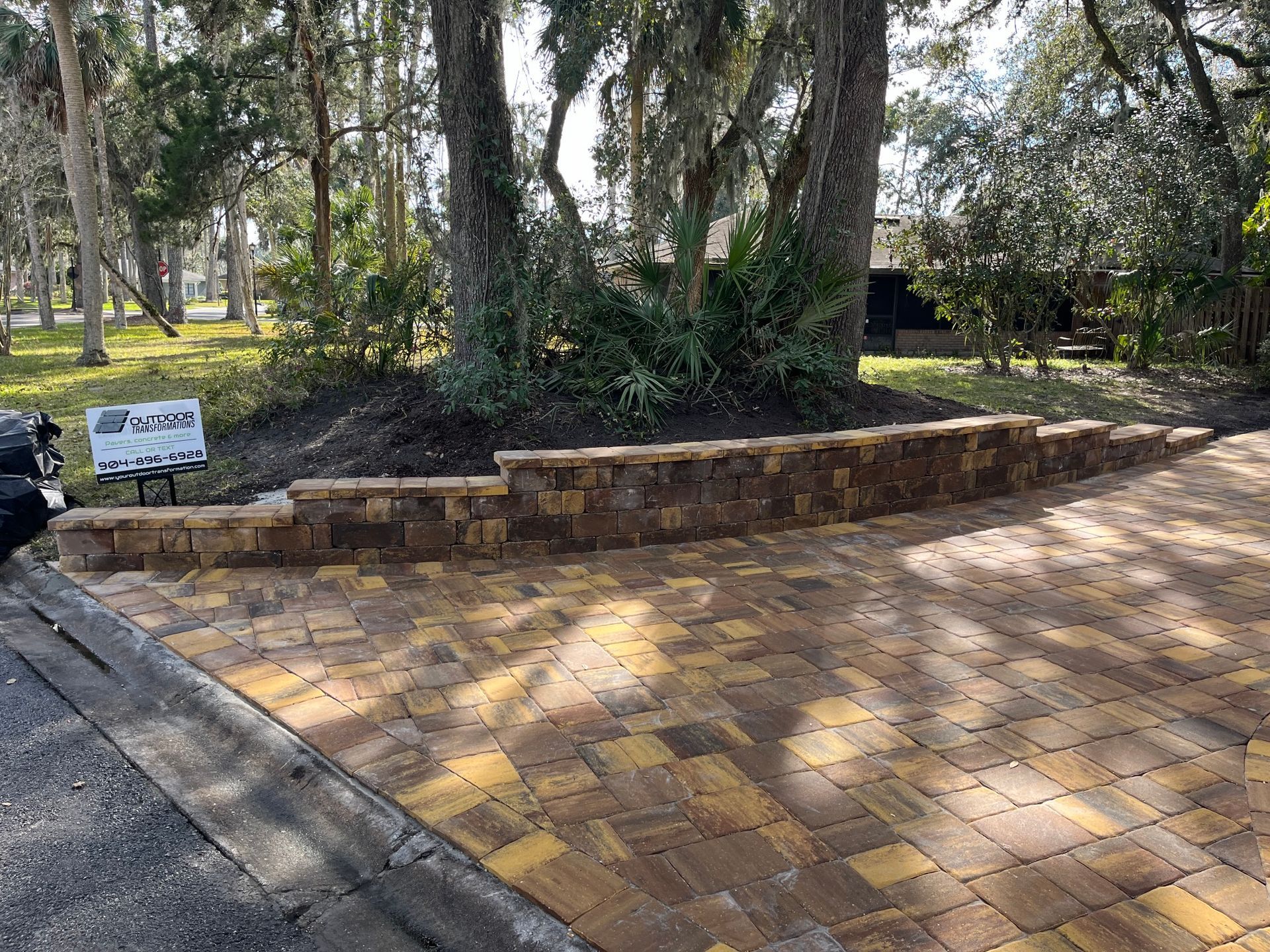A brick driveway with a stone wall and trees in the background.