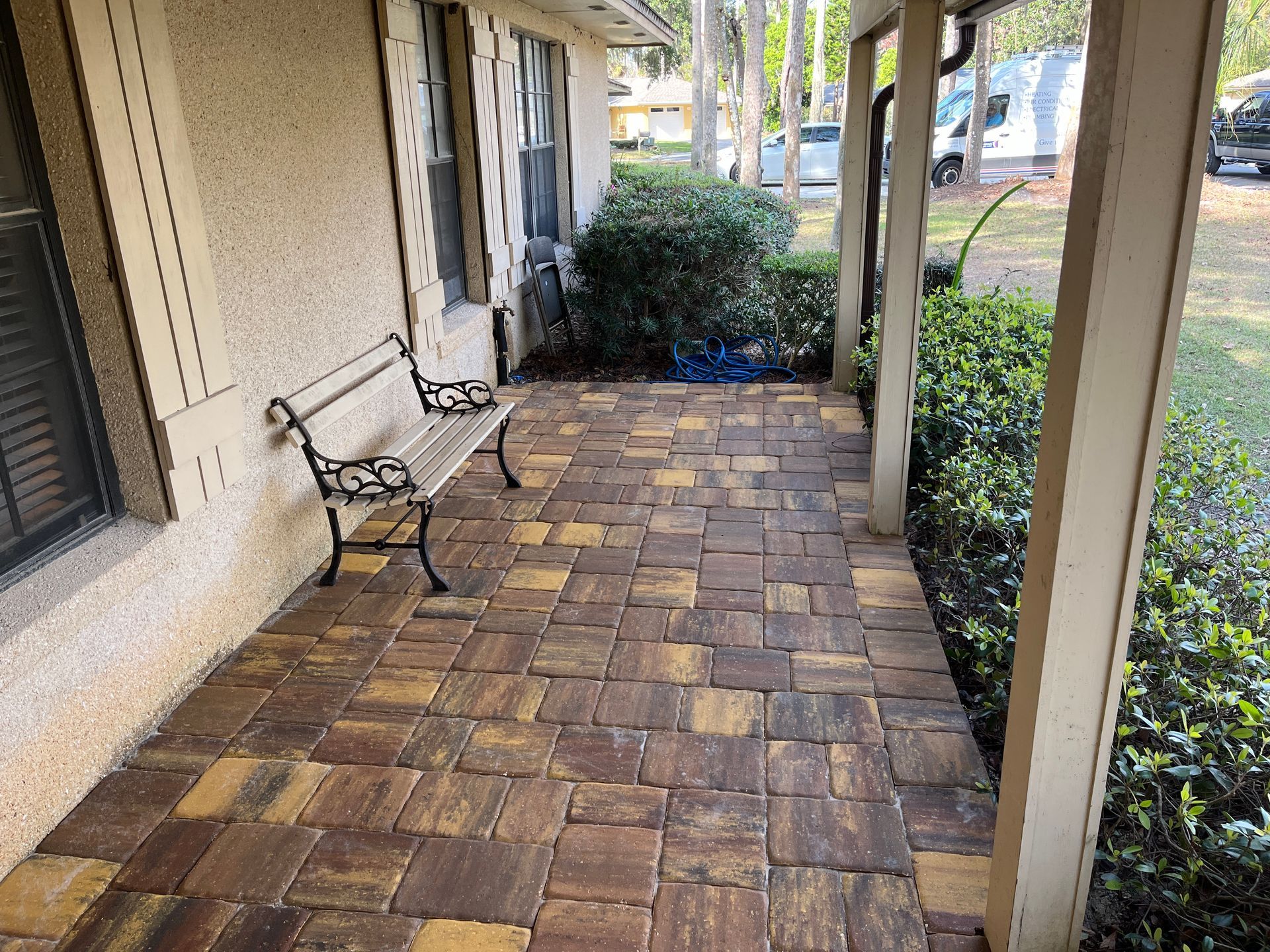 A stone-paved front porch with a metal bench next to a home exterior and landscaped shrubs.