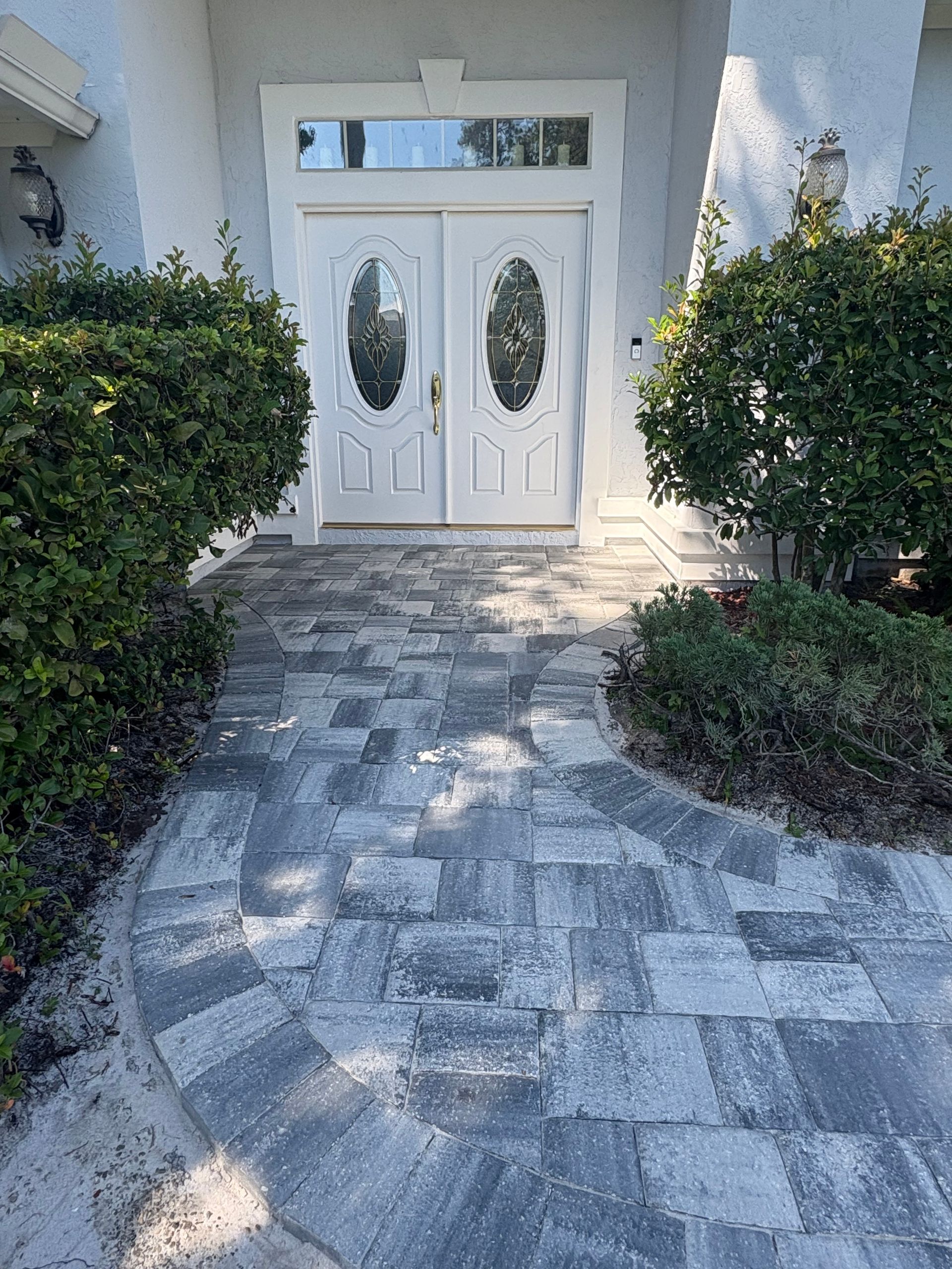 White double front door with oval glass panels, framed by trimmed hedges and a stone walkway.