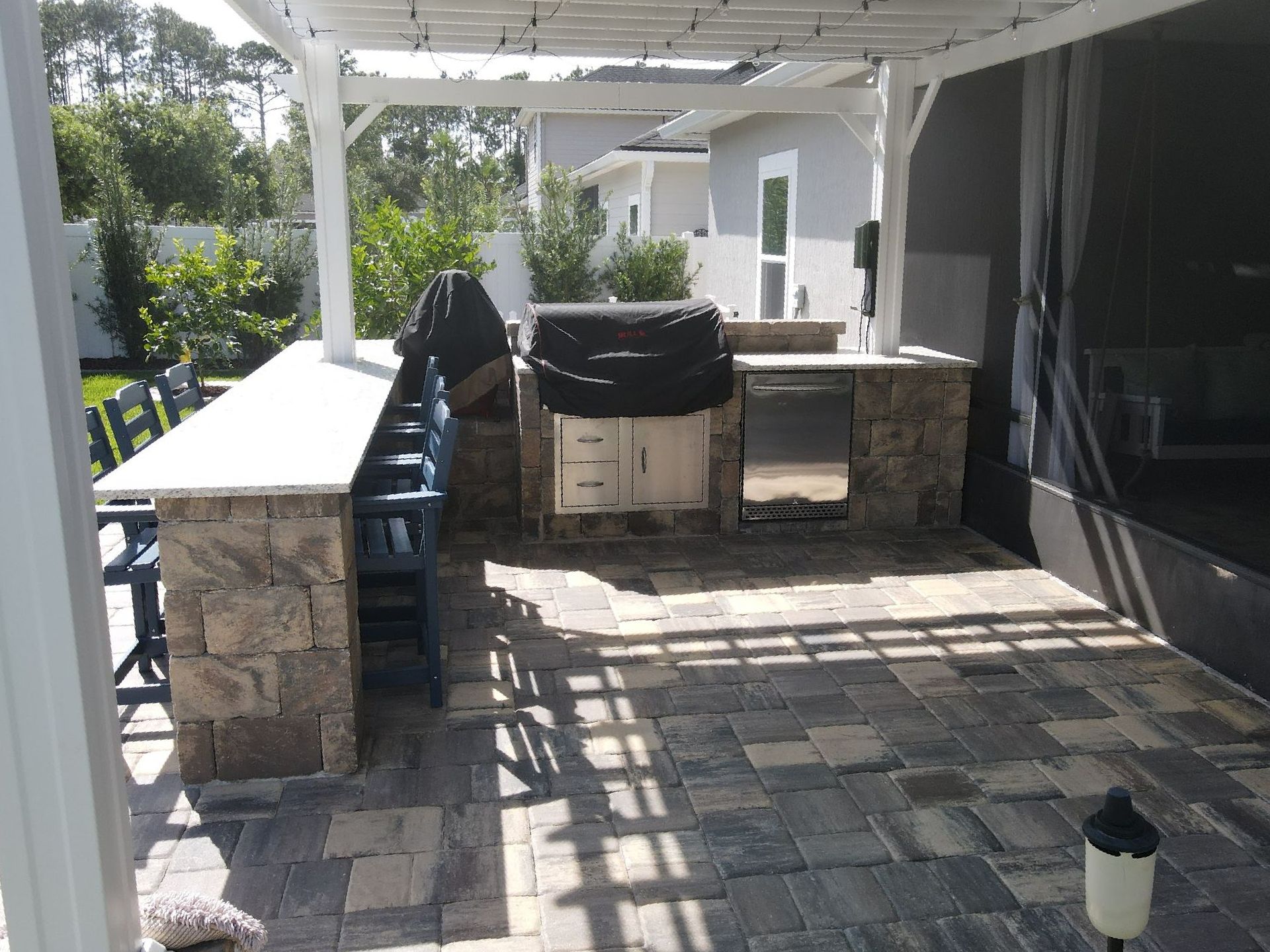 Covered patio with stone pavers, outdoor grill, long counter, and seating by a house