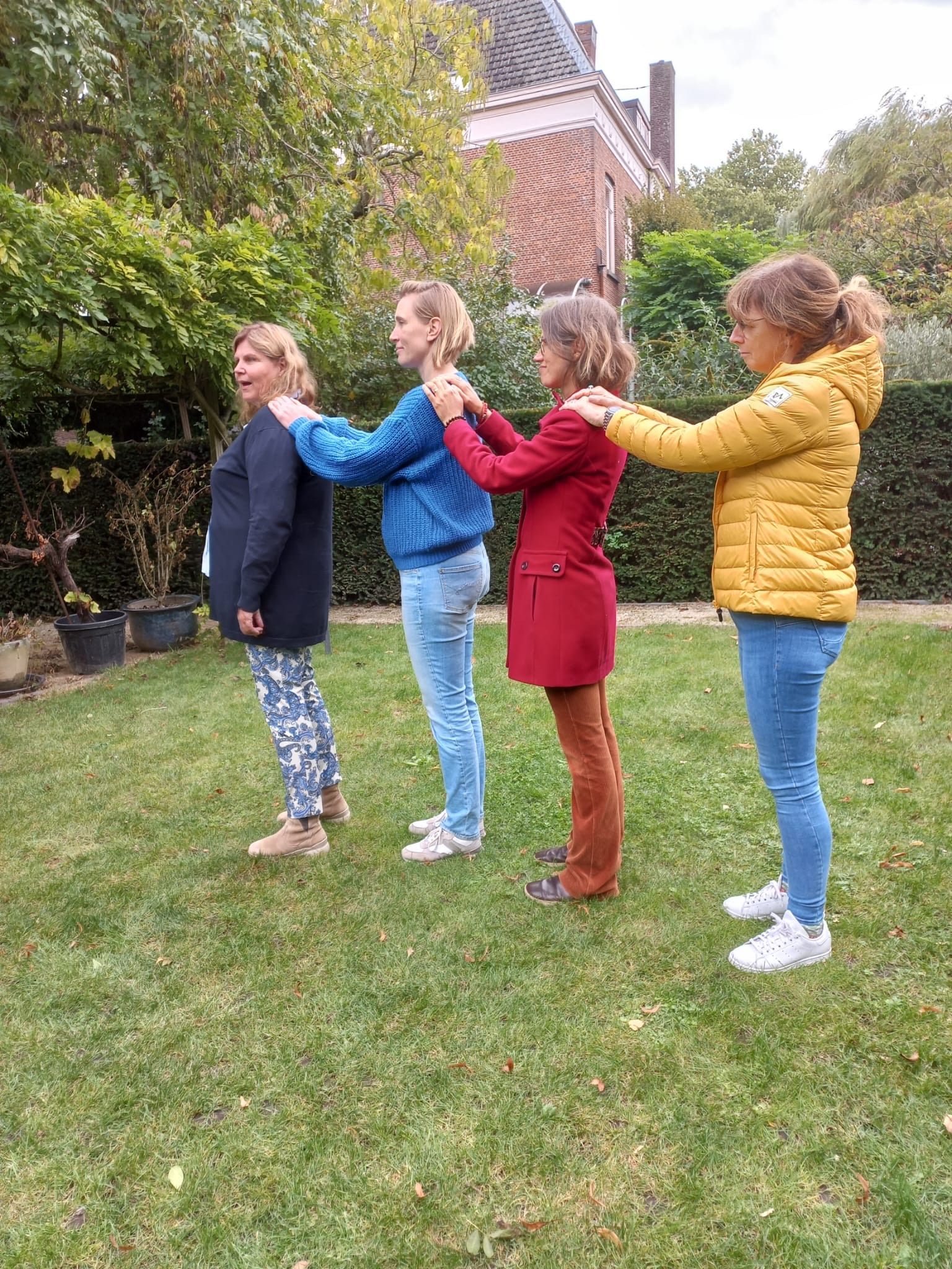 Vier vrouwen staan ​​op een rij, met hun handen op hun schouders, buiten op het gras.