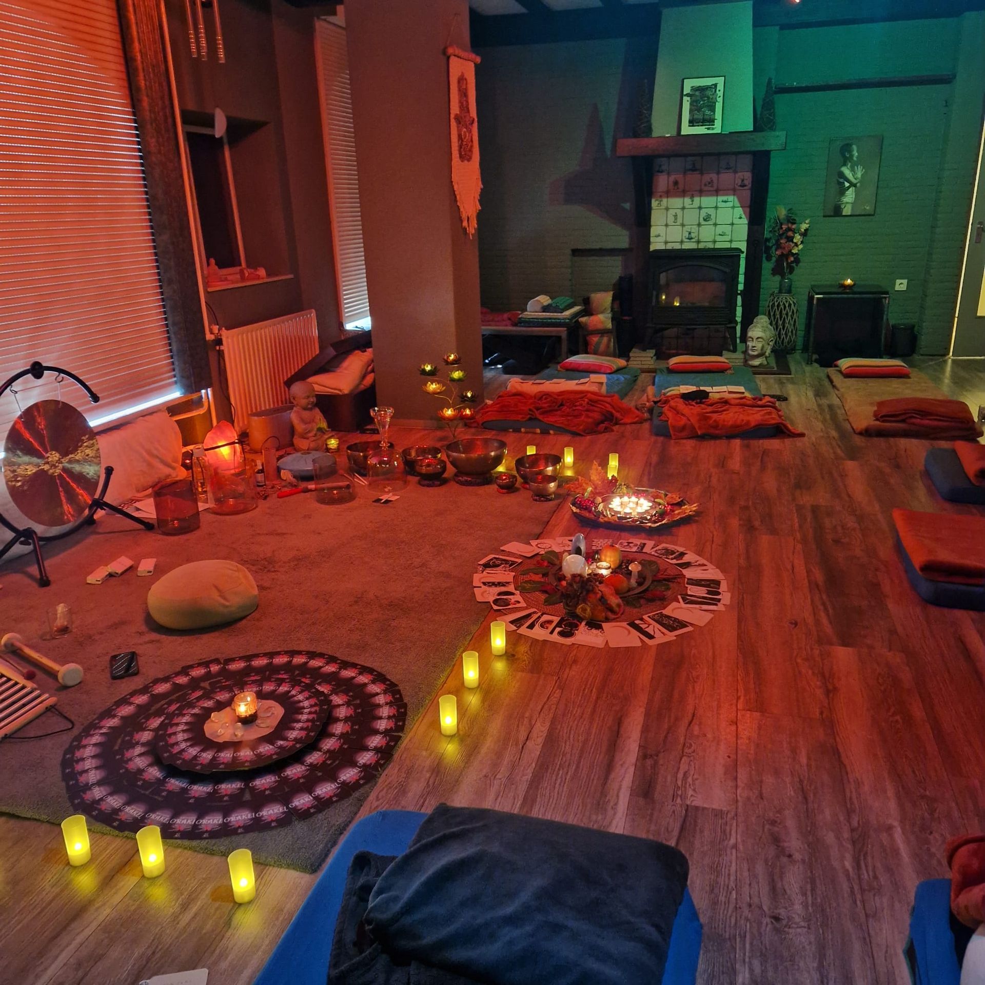 Een sfeervolle kamer met vloerkussens, kaarsen, vloerkleden met patronen en een kleine vuurplaats op een houten vloer.