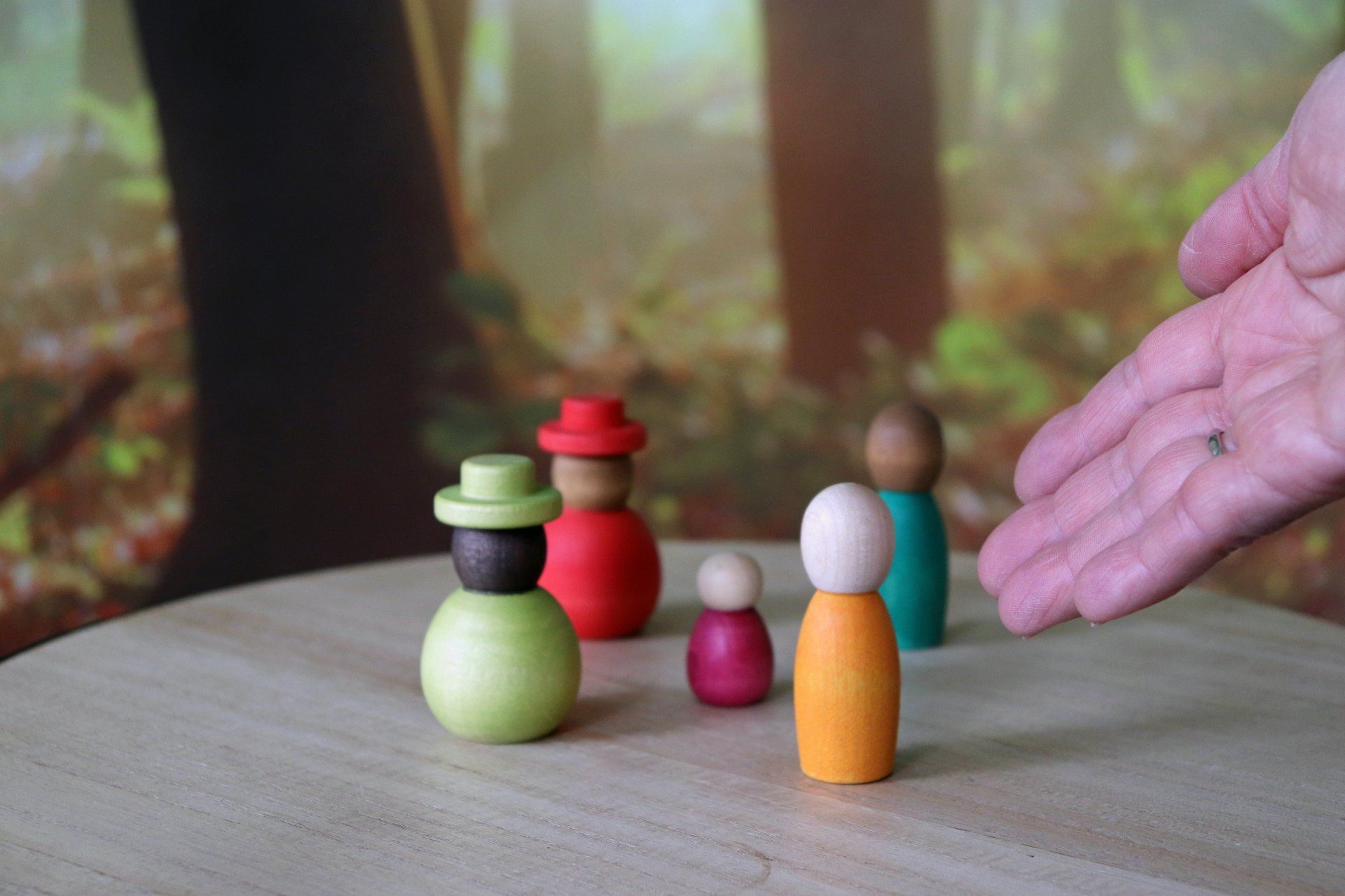 Houten figuren in een bosrijke omgeving; een hand reikt naar de groep.