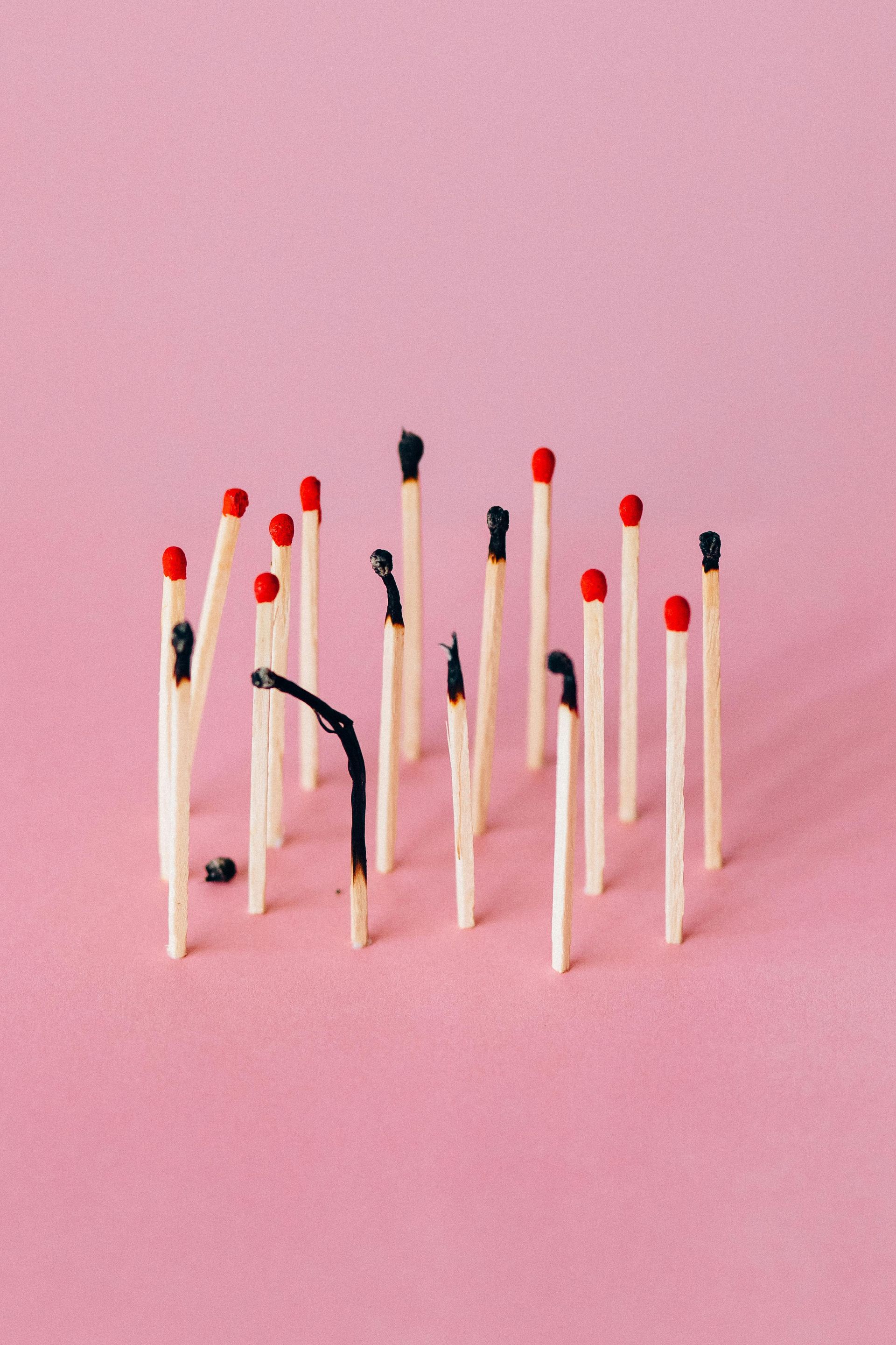 Lucifers, sommige opgebrand en sommige niet aangestoken, op een roze achtergrond.