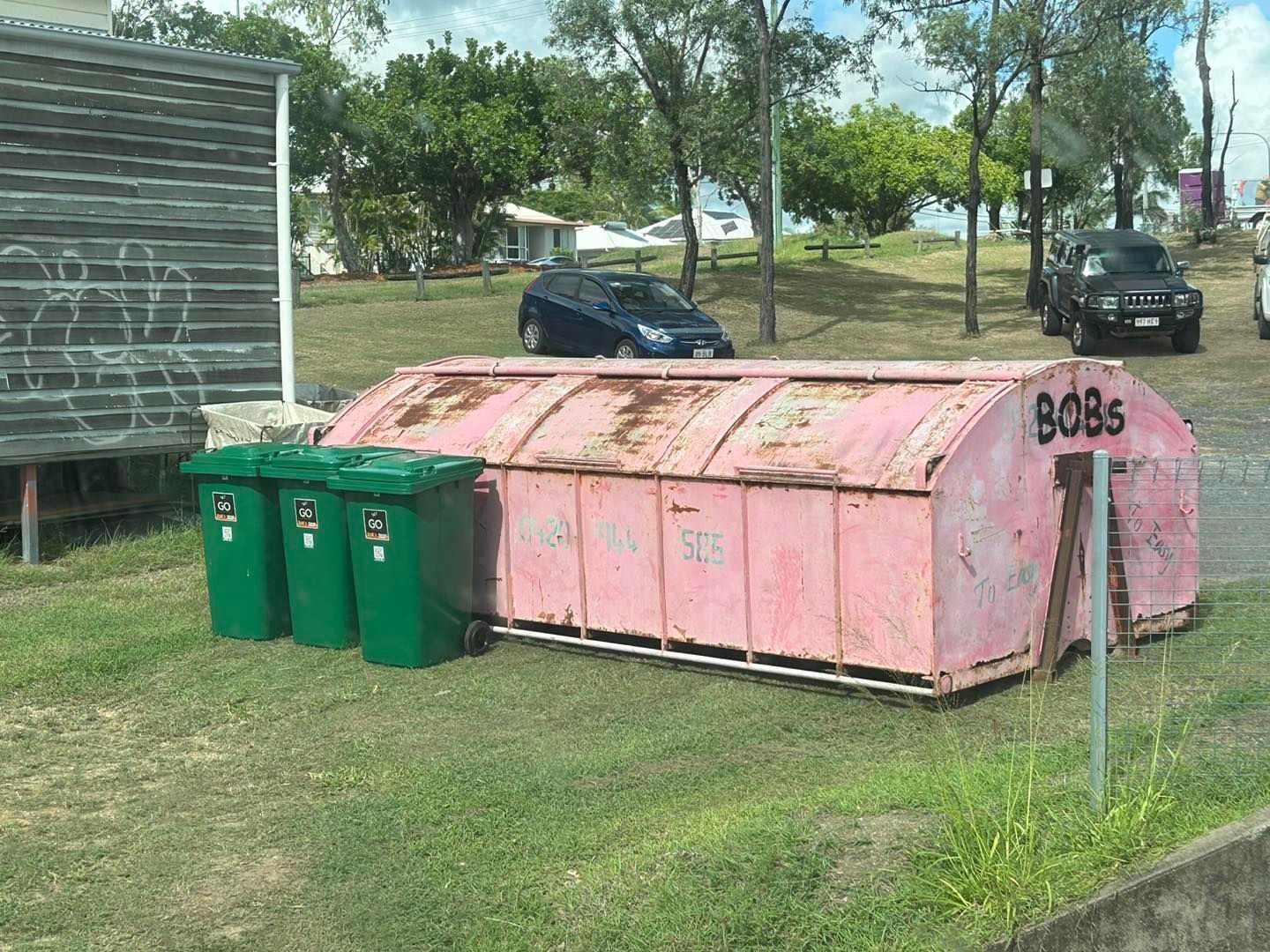 Pink Dumpster With Bobs Graffiti Next to Three Green Trash Bins — Bob’s Trailer Trash in Rockhampton, QLD