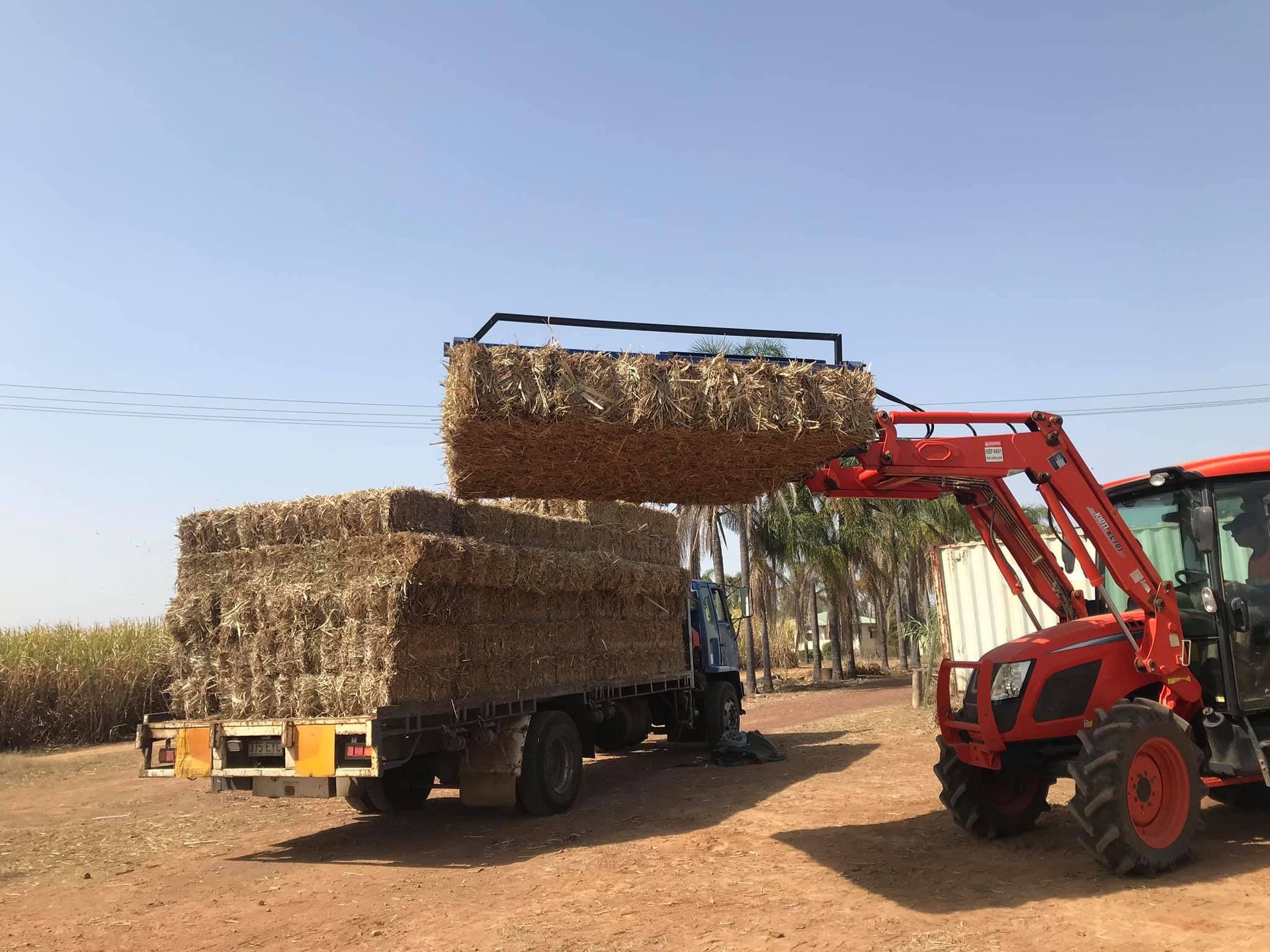 Red Tractor Loading Hay Bales Onto a Truck Bed on a Sunny Day — Bob’s Trailer Trash in Yeppoon, QLD