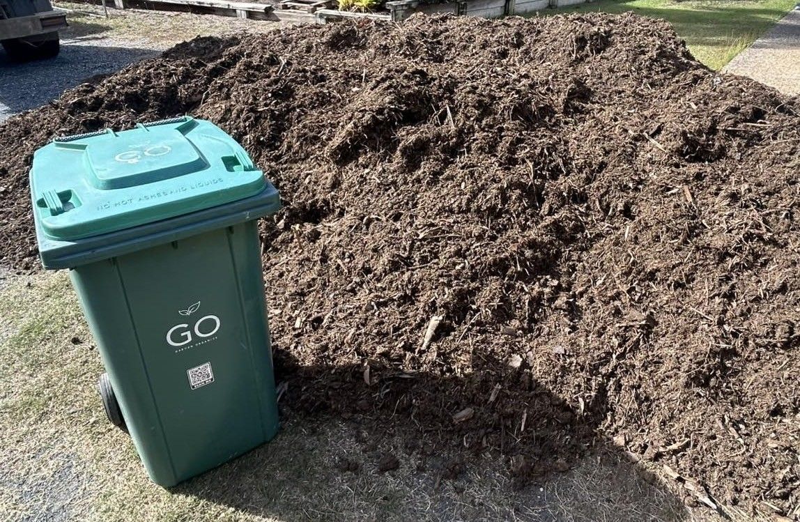 Green Trash Bin Beside a Large Pile of Brown Mulch on Grass — Bob’s Trailer Trash in Rockhampton, QLD