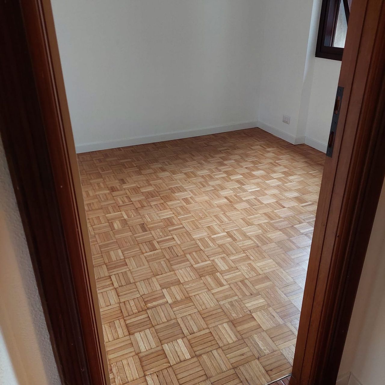 Stanza vuota con pavimento in parquet di legno chiaro, pareti bianche e vista sulla porta.