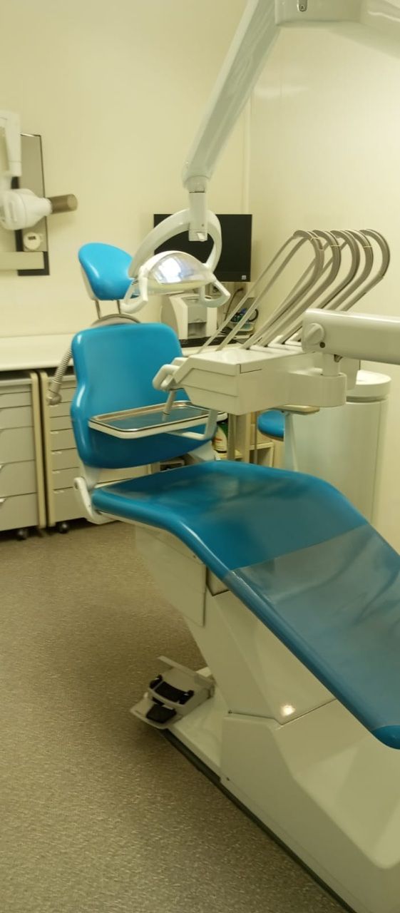 Poltrona odontoiatrica blu in una stanza clinica pulita con luce a soffitto e strumenti
