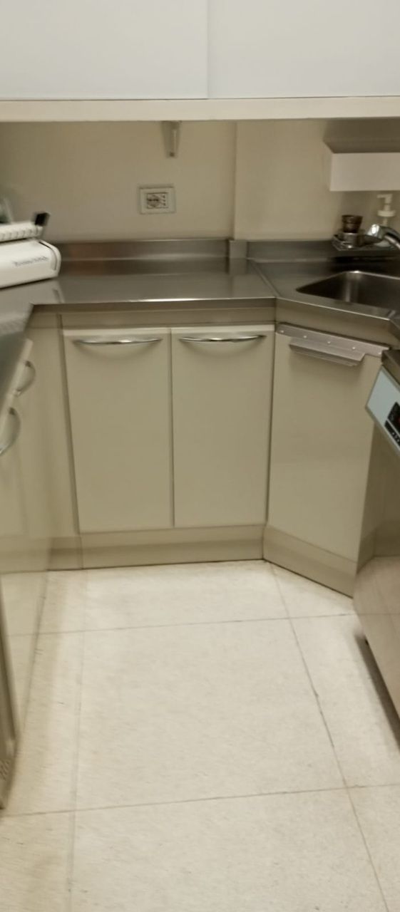 Piccolo angolo cottura beige con armadietti, piano di lavoro, lavello e pavimento piastrellato bianco in una stanza compatta