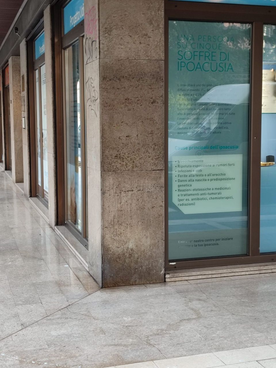 Corridoio in pietra con vetrine e un poster dai toni blu vicino all'ingresso.