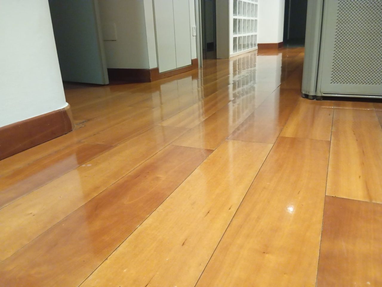 Pavimento in legno lucido nel corridoio con riflessi in una stanza interna luminosa