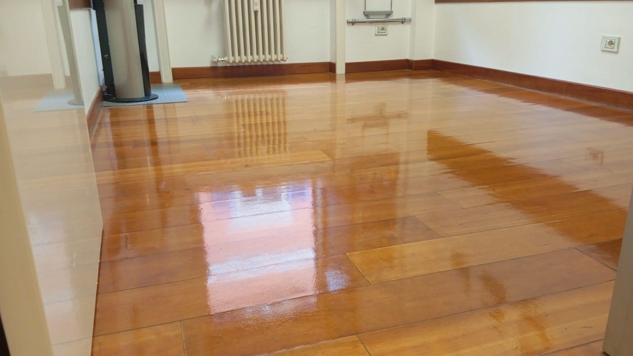 Pavimento in legno lucido in una stanza vuota con riflessi e un termosifone lungo la parete.