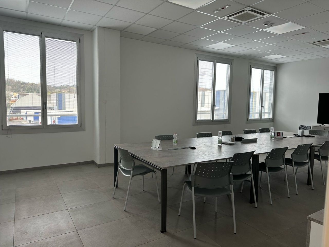 Sala conferenze vuota con un lungo tavolo, sedie nere e grandi finestre che lasciano entrare la luce naturale.