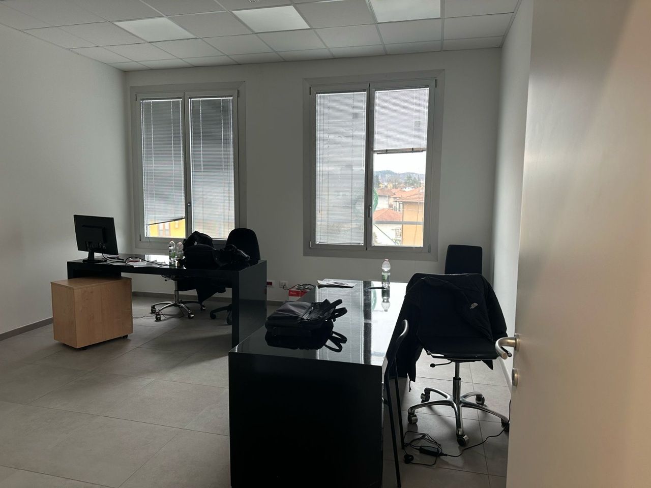 Ufficio vuoto con scrivanie, sedie, monitor e grandi finestre con vista sulla città.