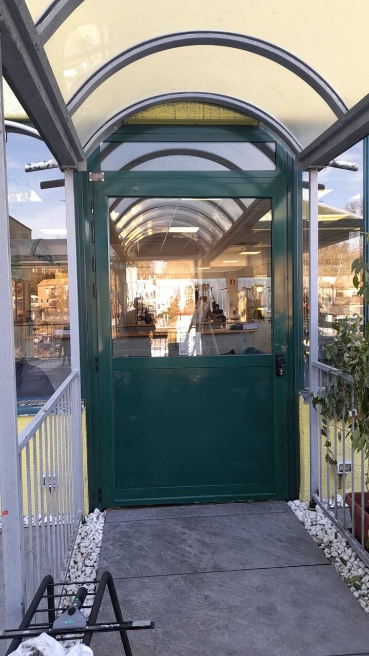 Un portale verde sotto una tettoia ad arco conduce all'ingresso illuminato di un edificio con pareti in vetro e una passerella.