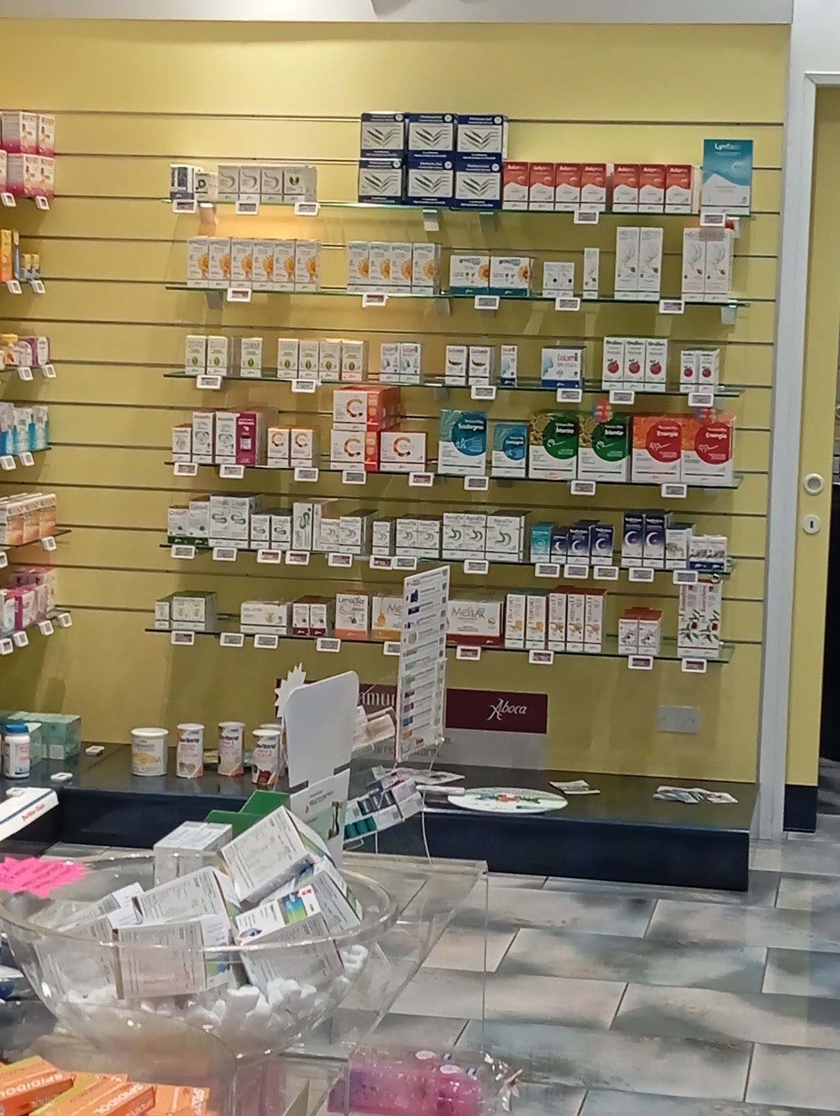 Parete della farmacia con file di scatole e flaconi di medicinali su scaffali sopra un contenitore di forniture.