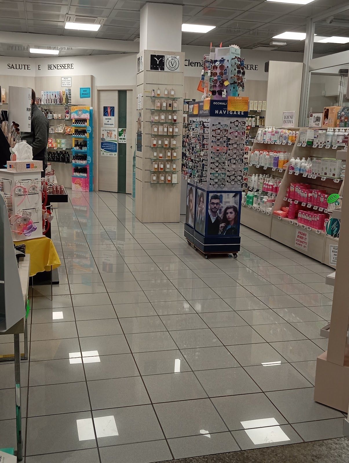 Corridoio del negozio ben illuminato con pavimento piastrellato, scaffali di cosmetici e un espositore centrale.