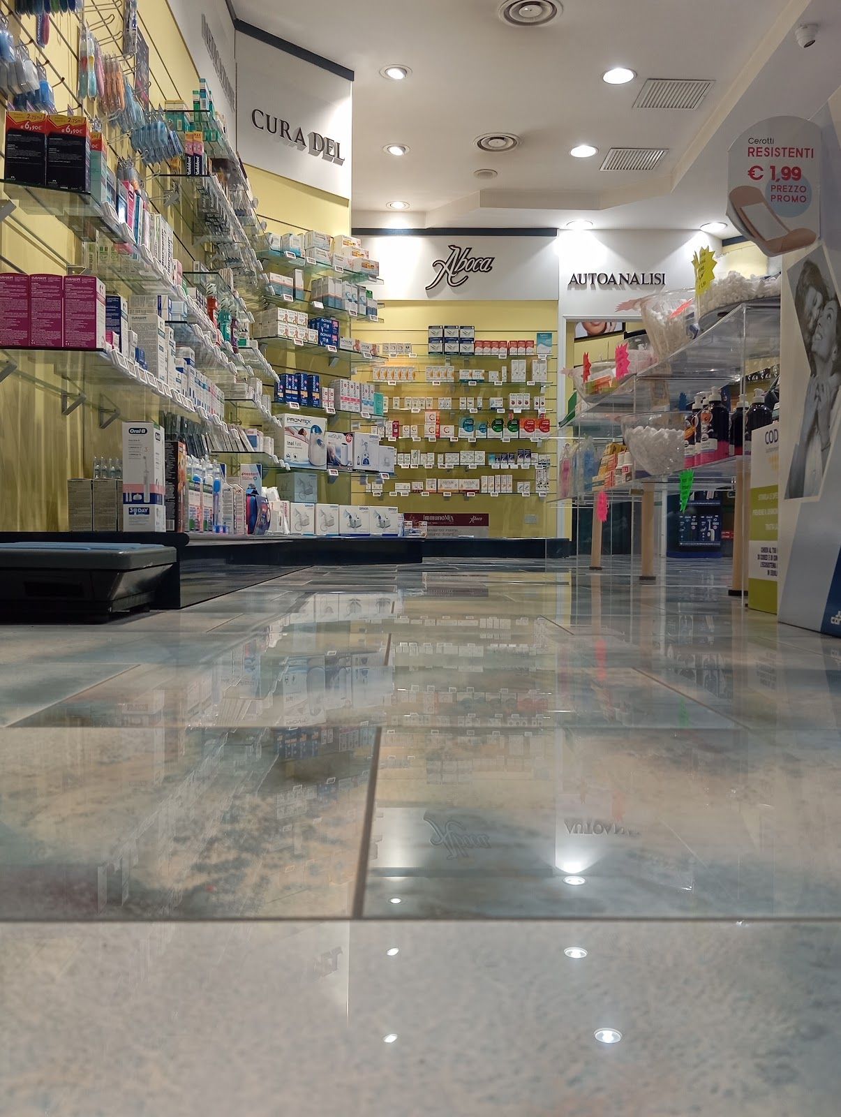Luminoso corridoio della farmacia con scaffali pieni di medicinali, pavimento piastrellato lucido e luci a soffitto.