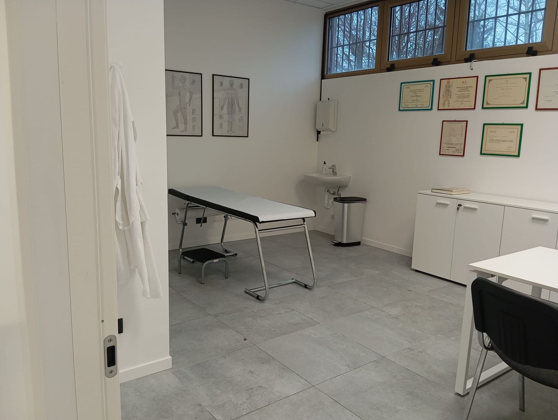 Piccola sala per le visite con lettino da visita, tavolo pieghevole, armadietti e cartelle cliniche a parete.