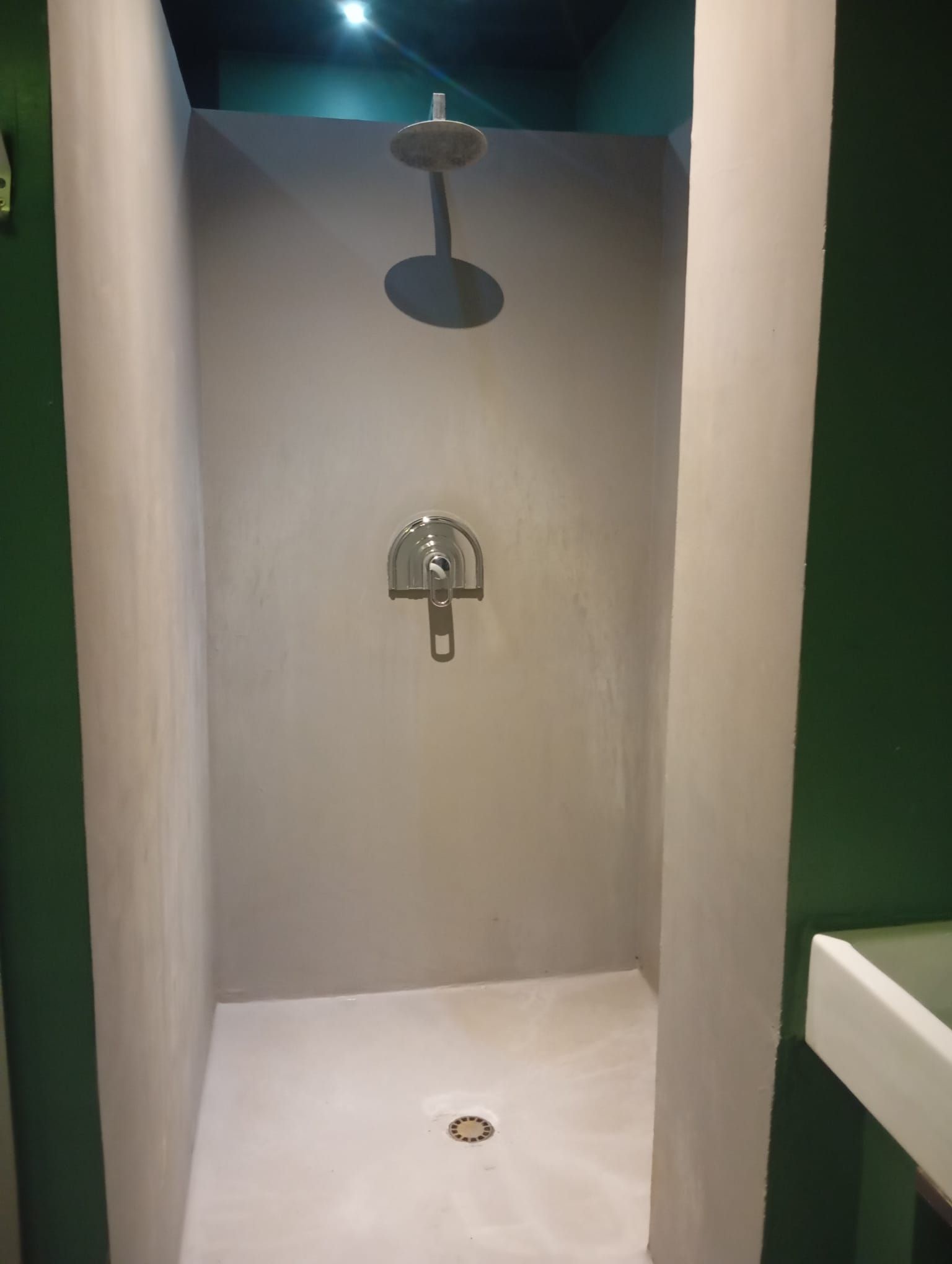 Box doccia pubblico vuoto con pareti grigie, pavimento bianco, soffione doccia e scarico a pavimento.