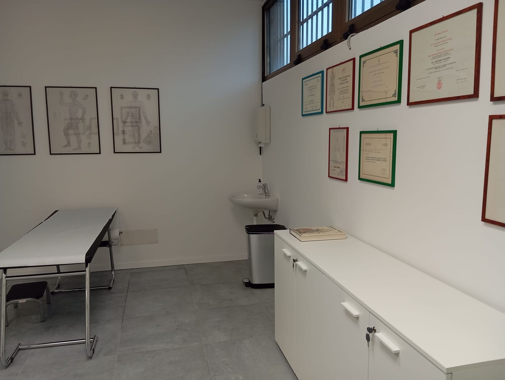 Aula vuota con tavoli bianchi, poster alle pareti, un lavandino e una parete superiore con finestre.