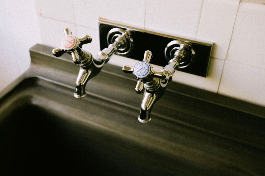 Two chrome sink faucets above a dark stainless steel basin against white tile