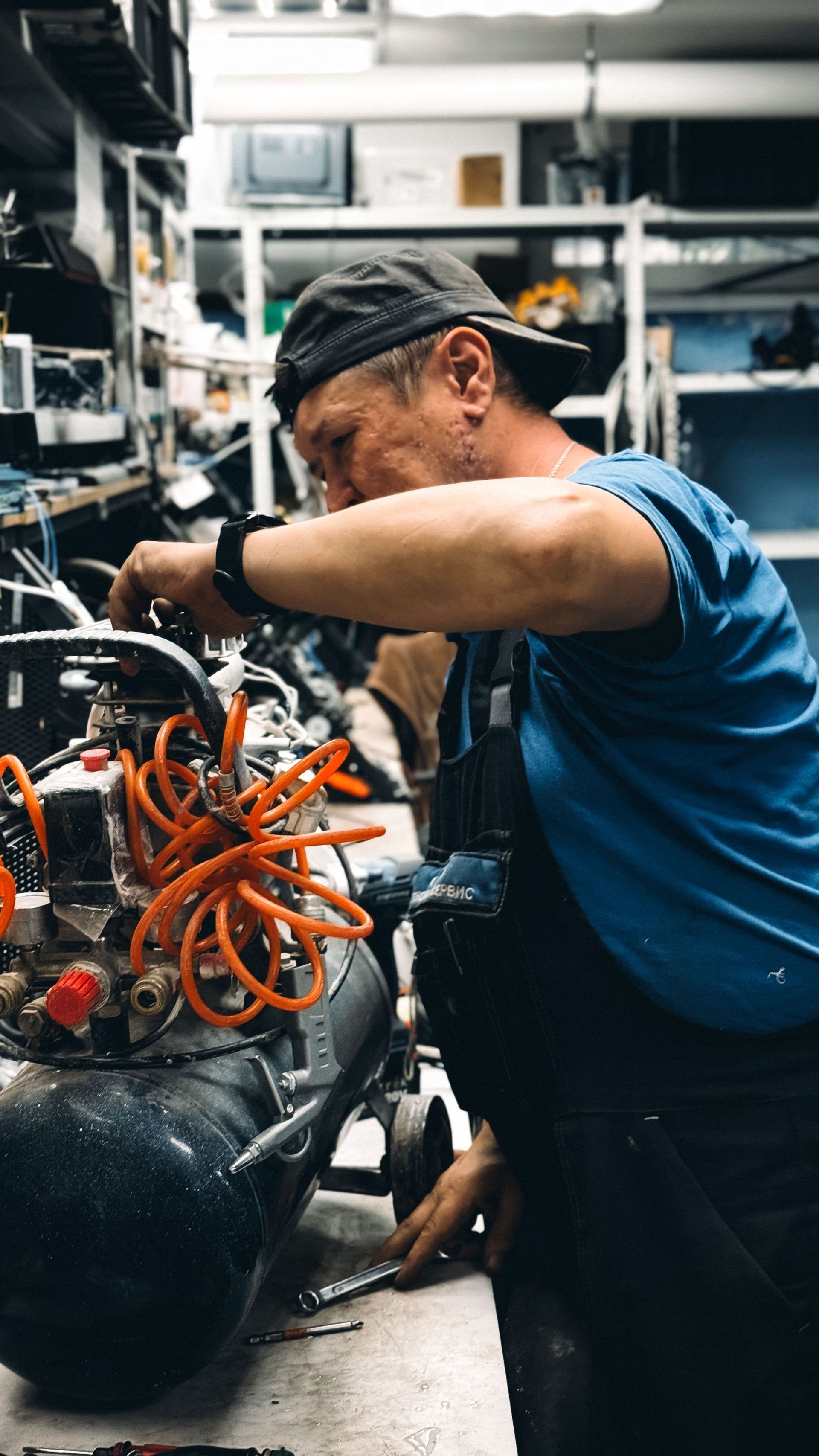 Mechanic in blue shirt working on machinery with orange cables in an industrial workshop