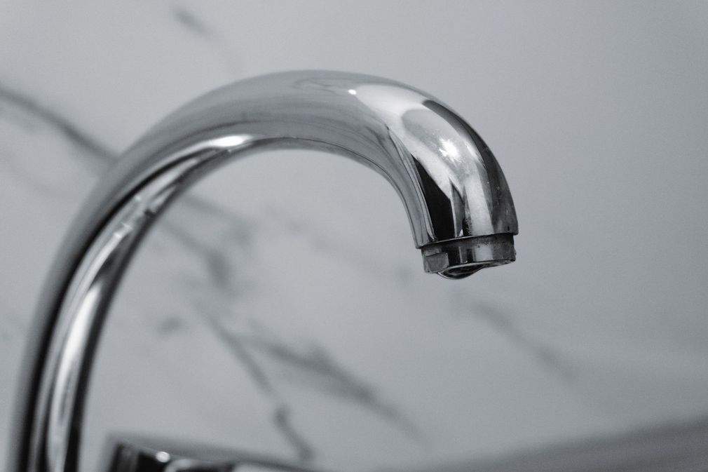 Chrome faucet spout over a marble sink wall
