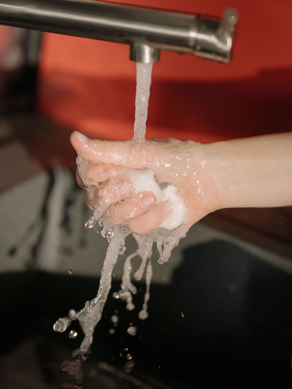 Hand under running faucet, washing with water splashing into a sink.