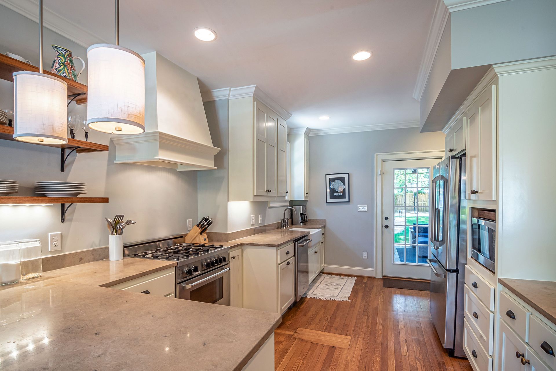 Bright modern kitchen with white cabinets, marble counters, gas stove, and wood floors